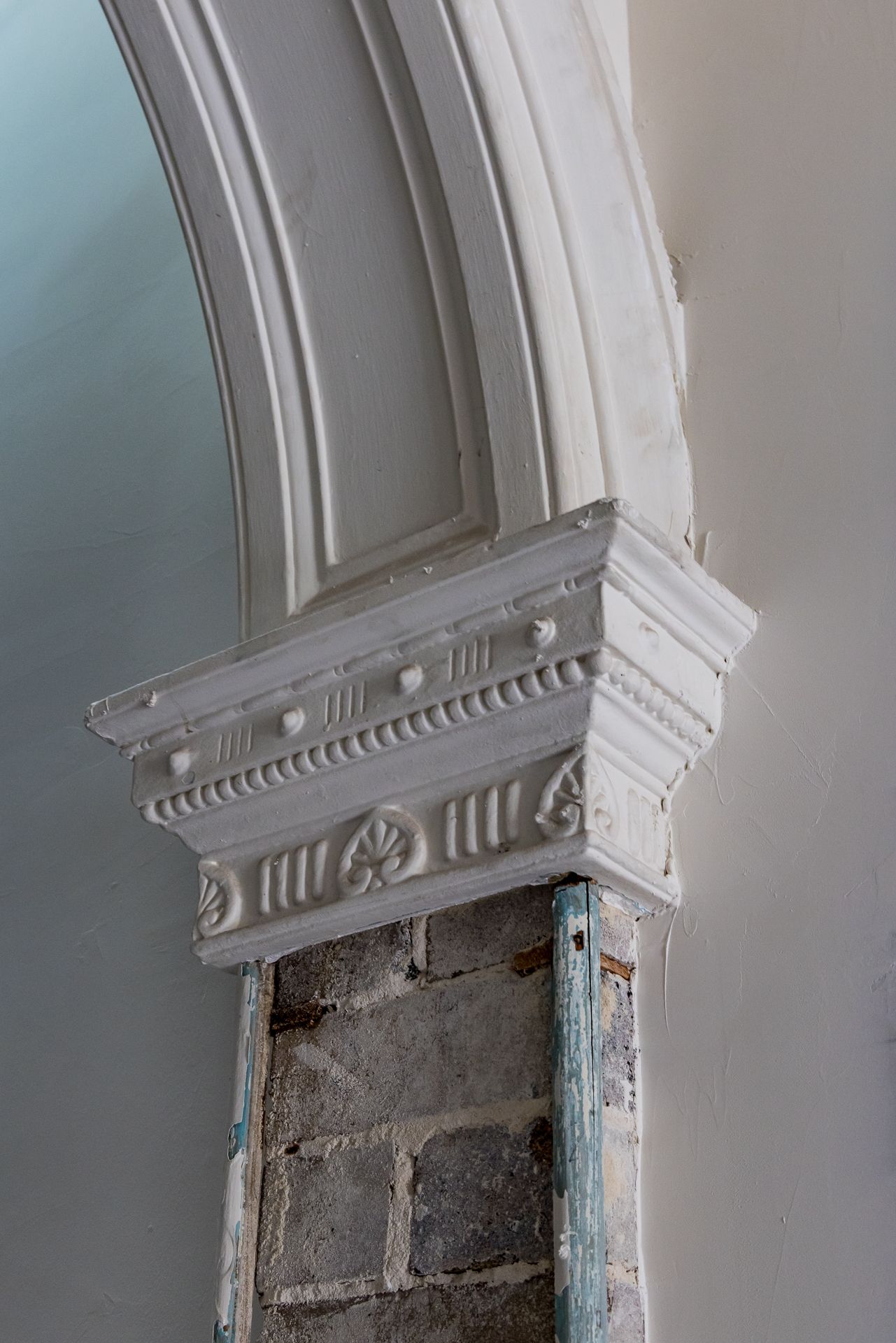 Close-up of an ornate white plaster arch capital with decorative rosettes above exposed brick, in a heritage building.