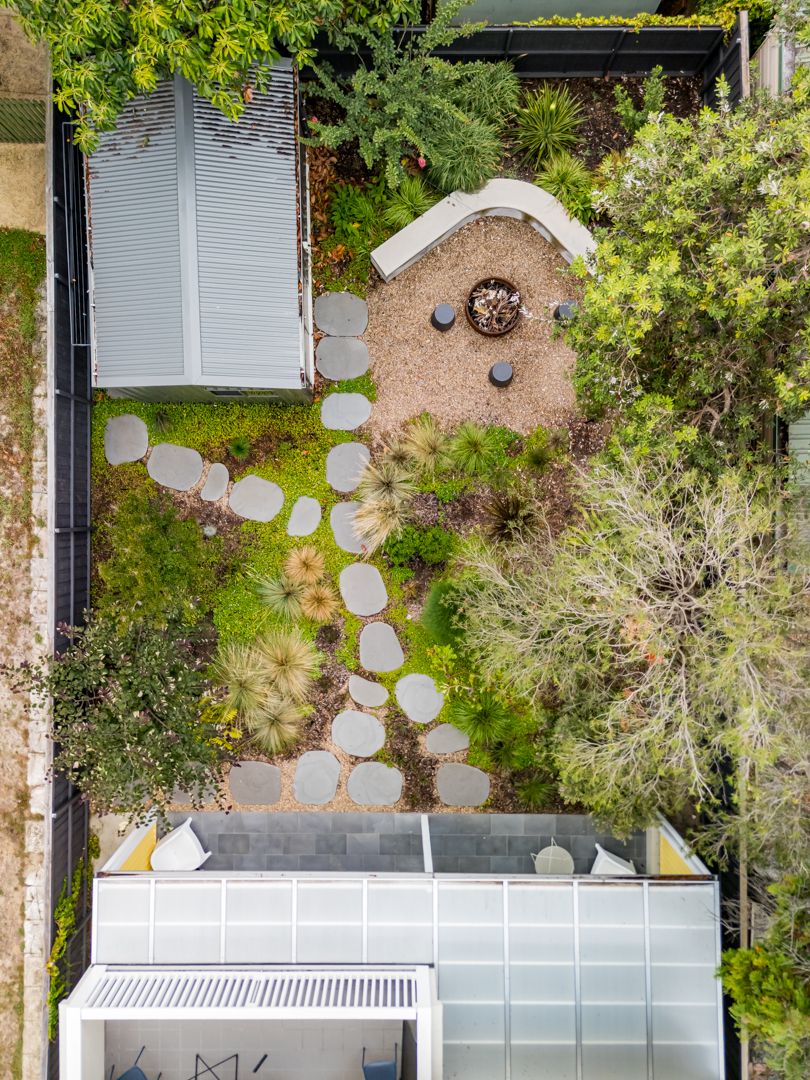 Aerial view of a landscaped garden with stepping stones, a circular fire pit, curved seat and native plants beside a small studio.
