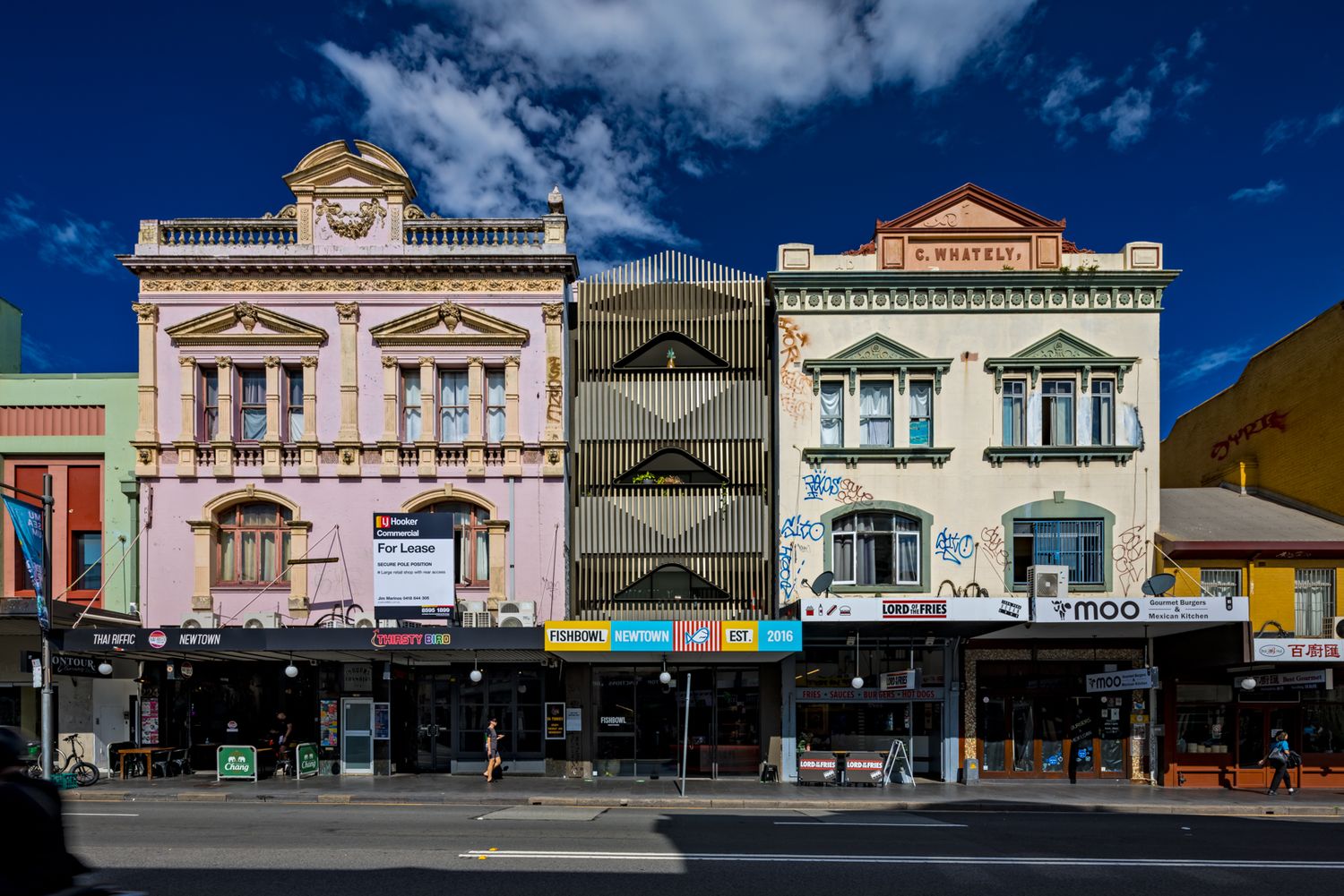 Colorful heritage shopfronts with ornate Victorian facades and street-level stores beneath a deep blue sky with scattered clouds.