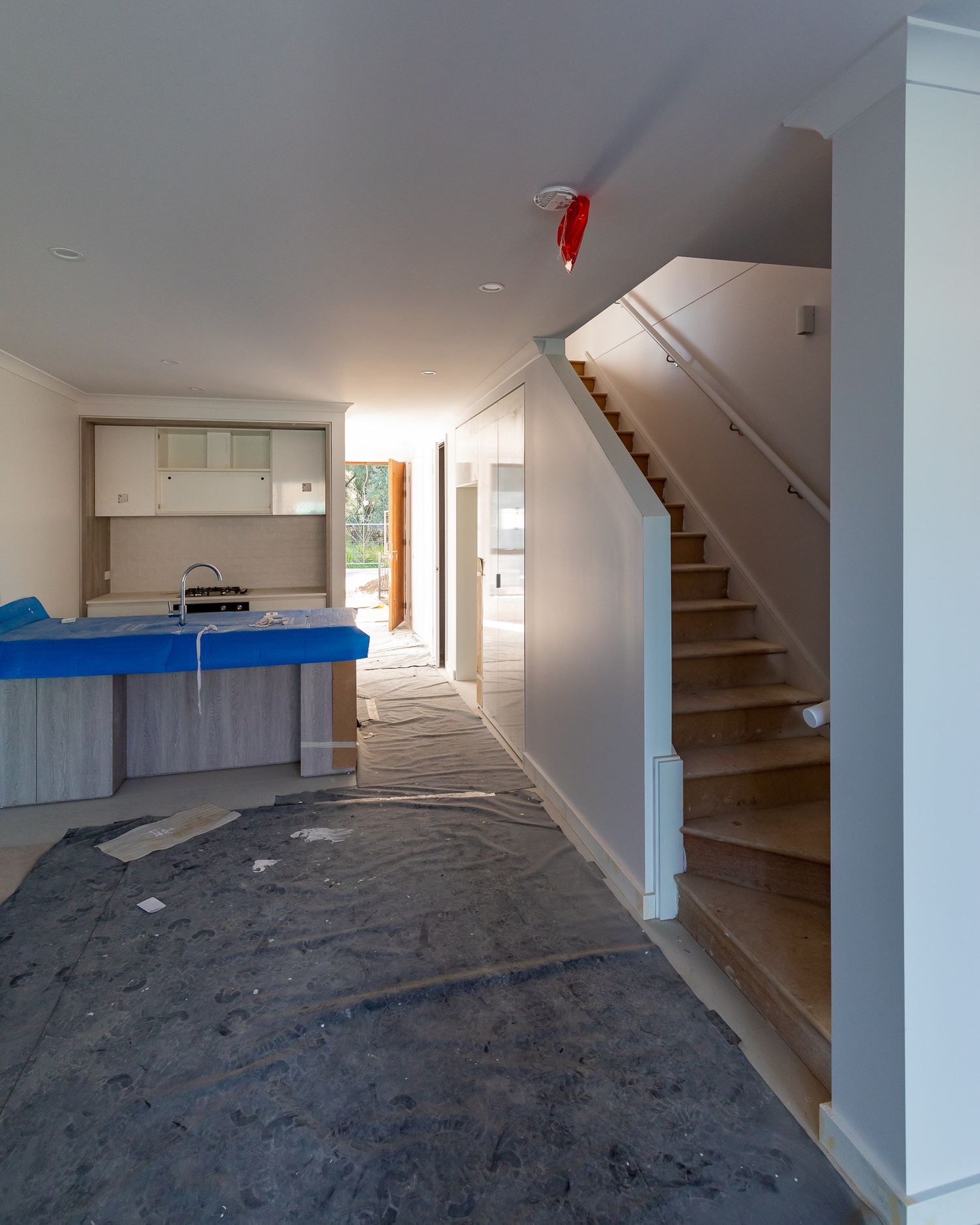 Unfinished home interior with protective floor covering, a blue-wrapped kitchen island, and a timber staircase under construction.