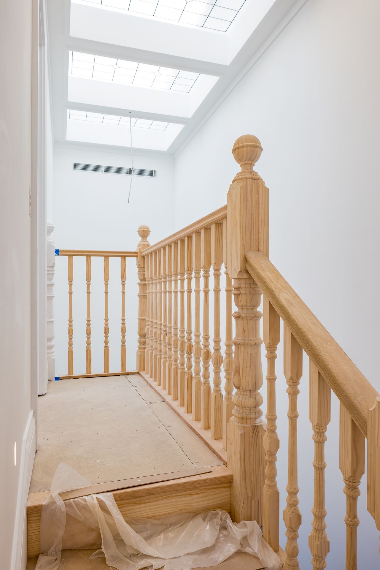 Newly built timber staircase with turned balusters and a carved newel post leading up toward a bright skylight in a home renovation.