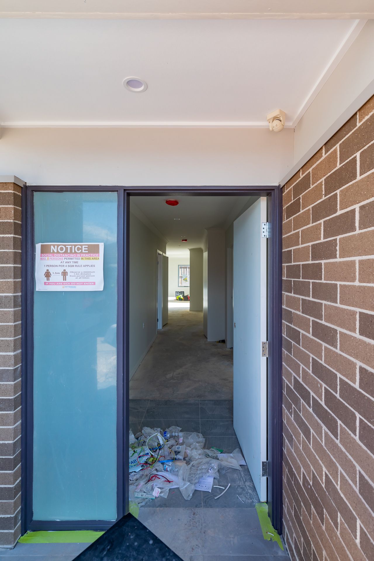 Open front doorway of an unfinished brick townhouse with a safety notice on the glass and builders' debris on the floor.