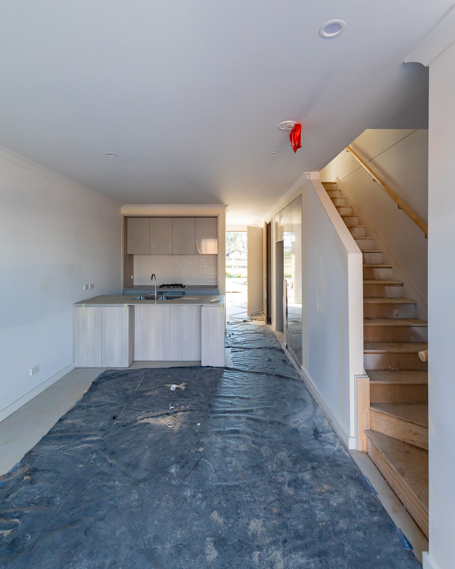 Open-plan townhouse interior under construction with kitchen, timber staircase and protective plastic covering the floor.