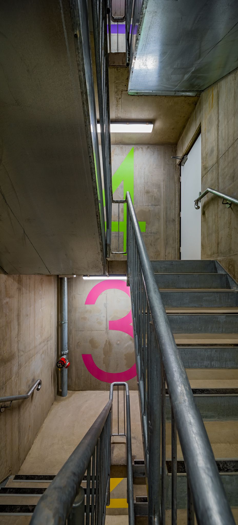 Concrete stairwell with metal handrails and bold pink number 3 and green number 1 painted on the walls for floor wayfinding.