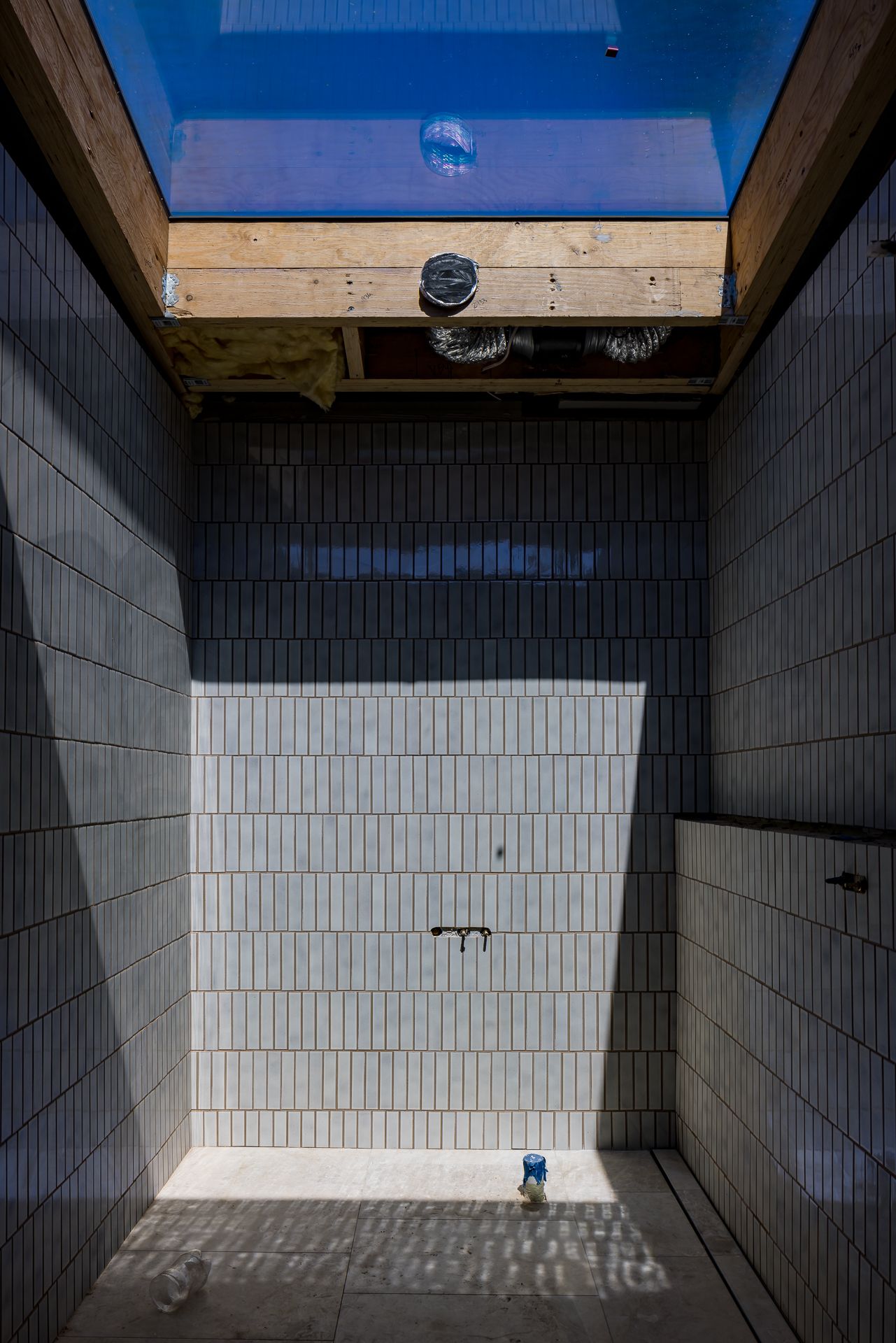 Unfinished tiled shower recess with vertical gray tiles, a wall-mounted tap and a bright skylight overhead.