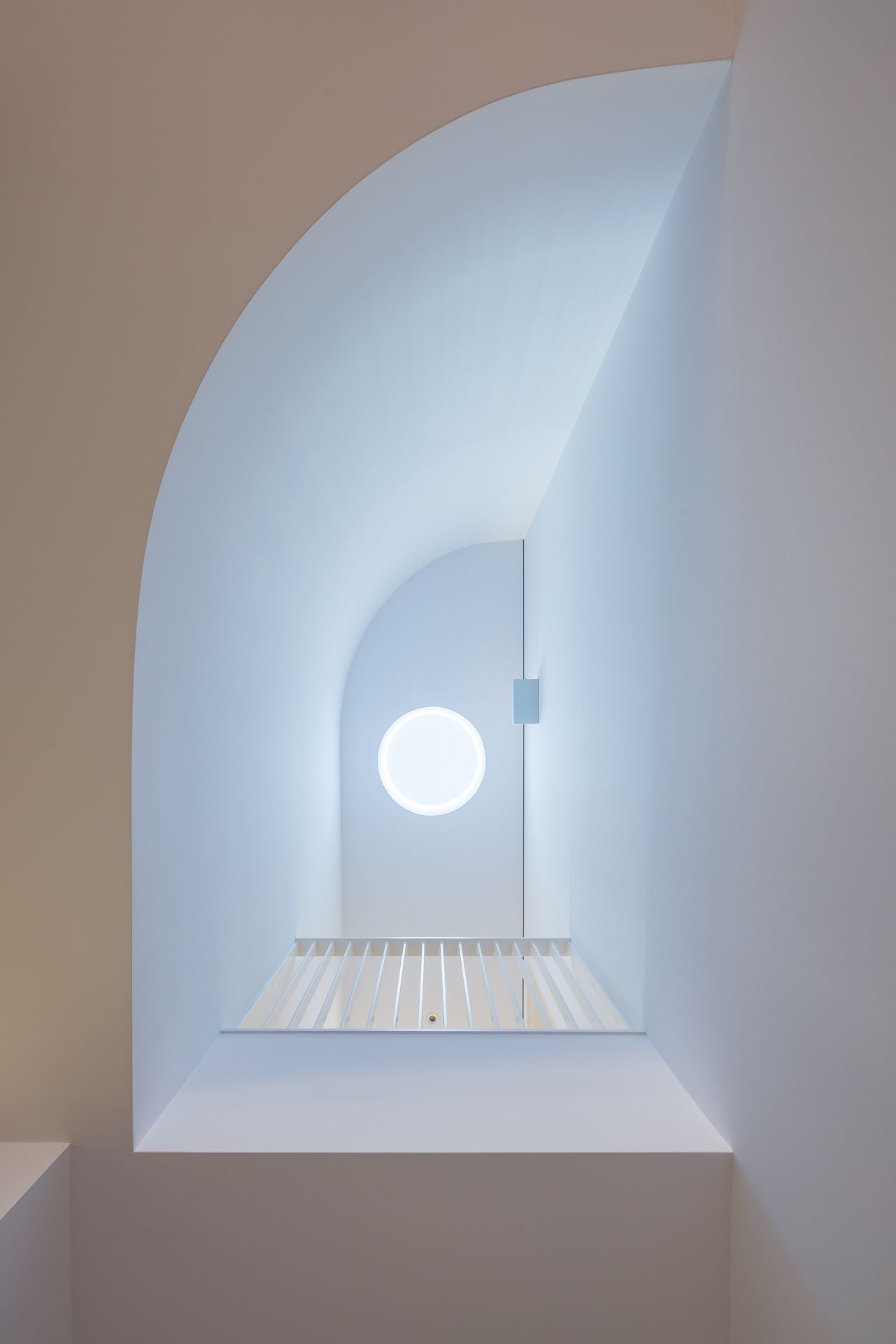 Curved white archway stairwell with a circular skylight casting soft light over a slatted timber landing.