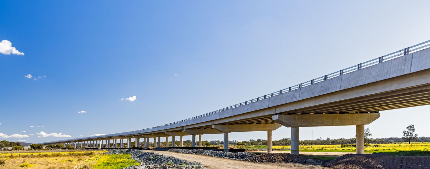 Long elevated concrete highway bridge curving across open grassland under a bright blue sky.