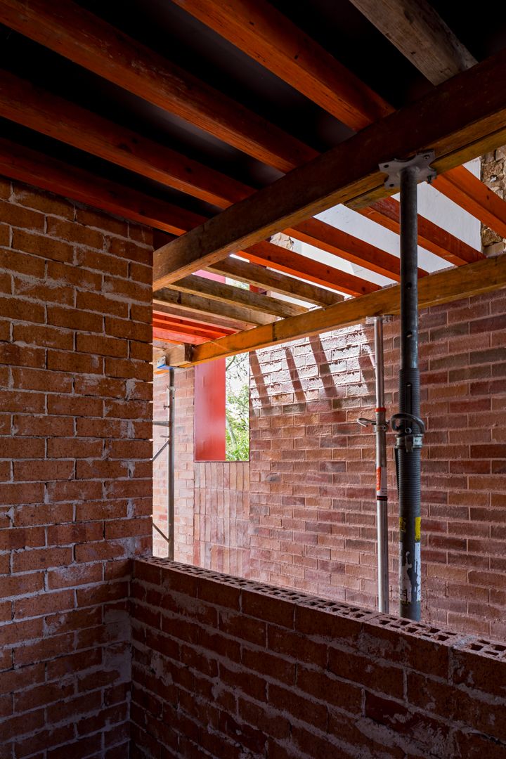 Exposed red brick walls and timber ceiling joists supported by steel props inside a building under renovation.