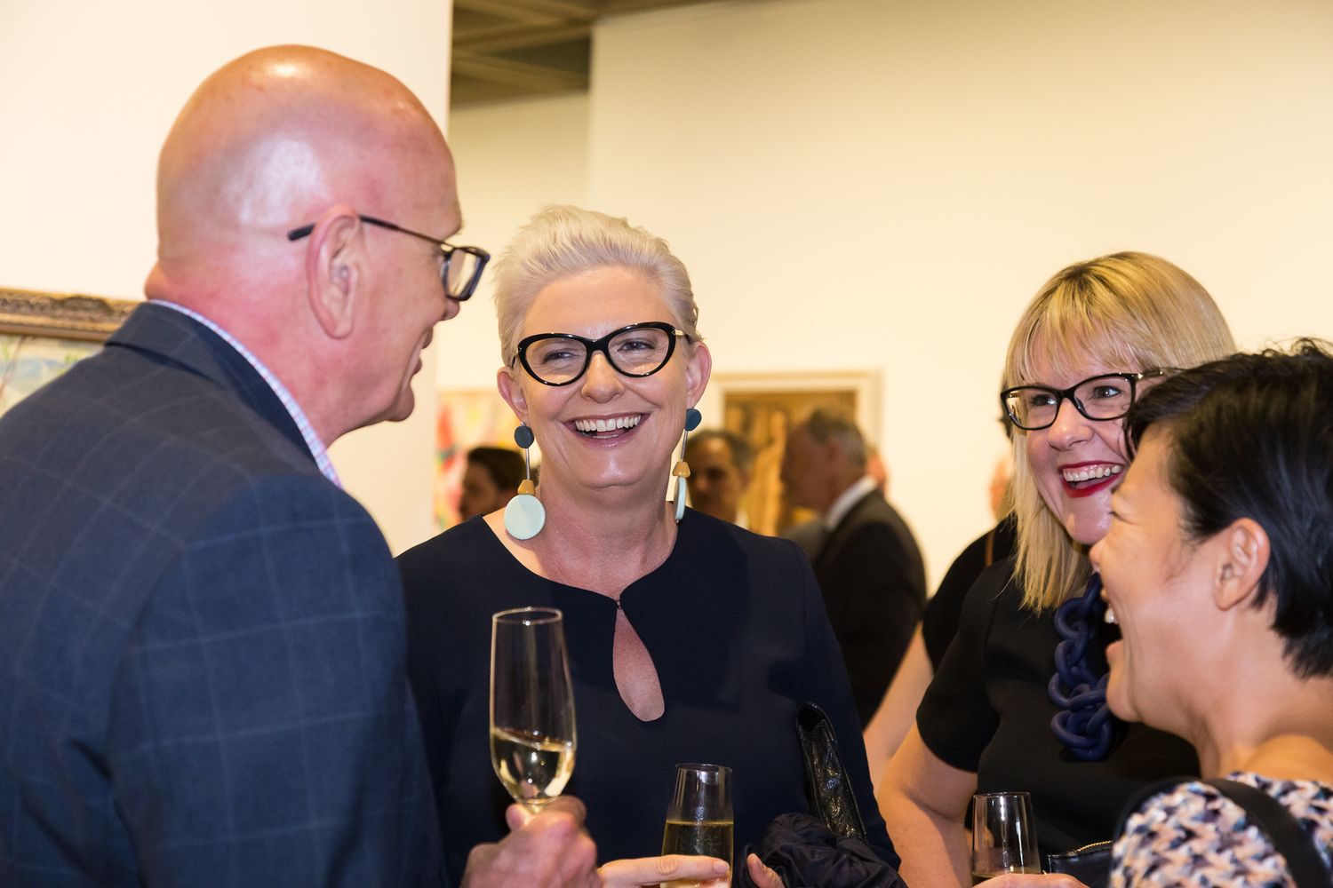 Guests smile and chat while holding champagne glasses at an art gallery event.