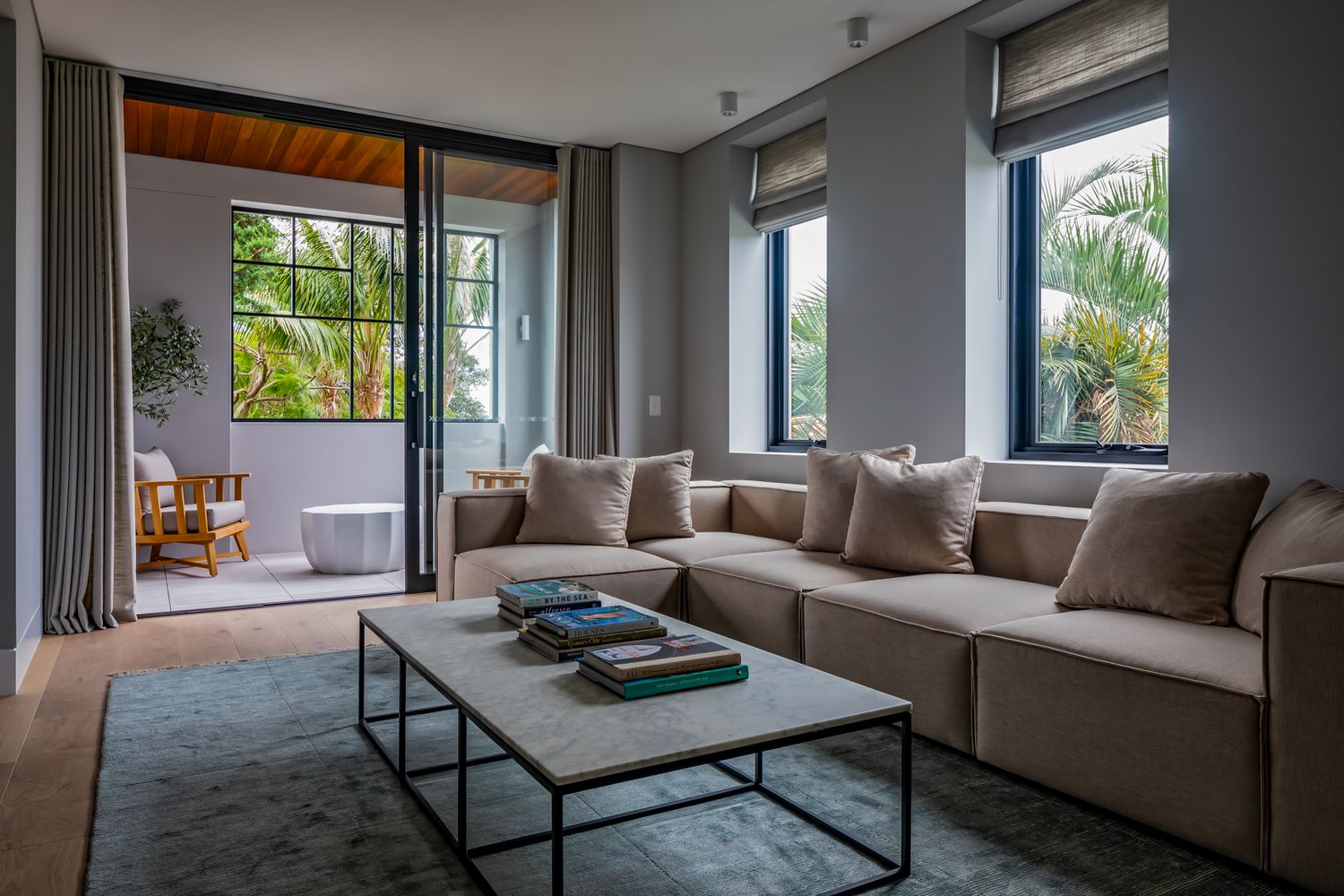 Cosy living room with a beige sectional sofa, steel-framed coffee table and sliding doors opening to a palm-lined patio.