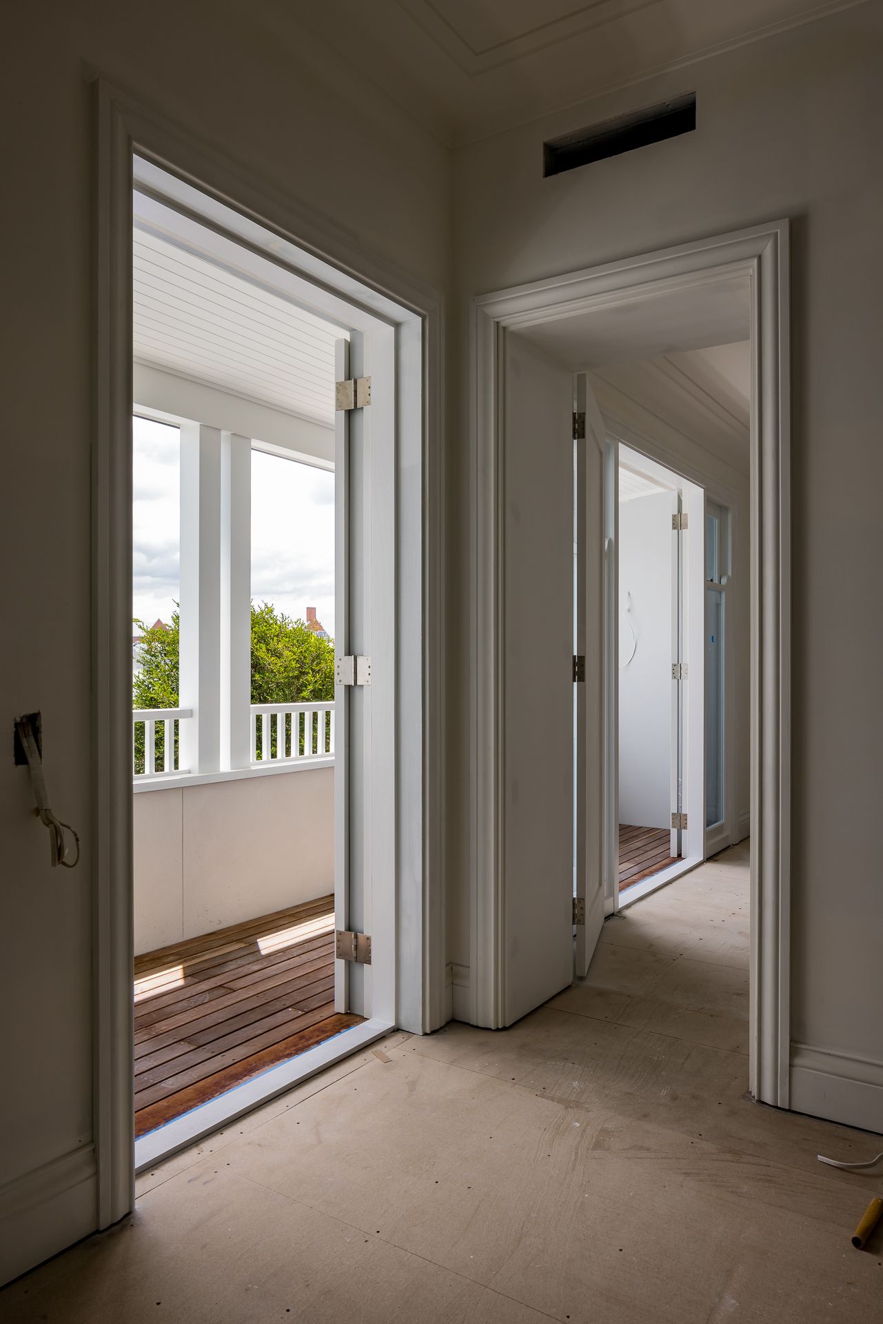 Upstairs hallway with white doorways leading to a sunny timber-floored balcony and another room in a renovated home.
