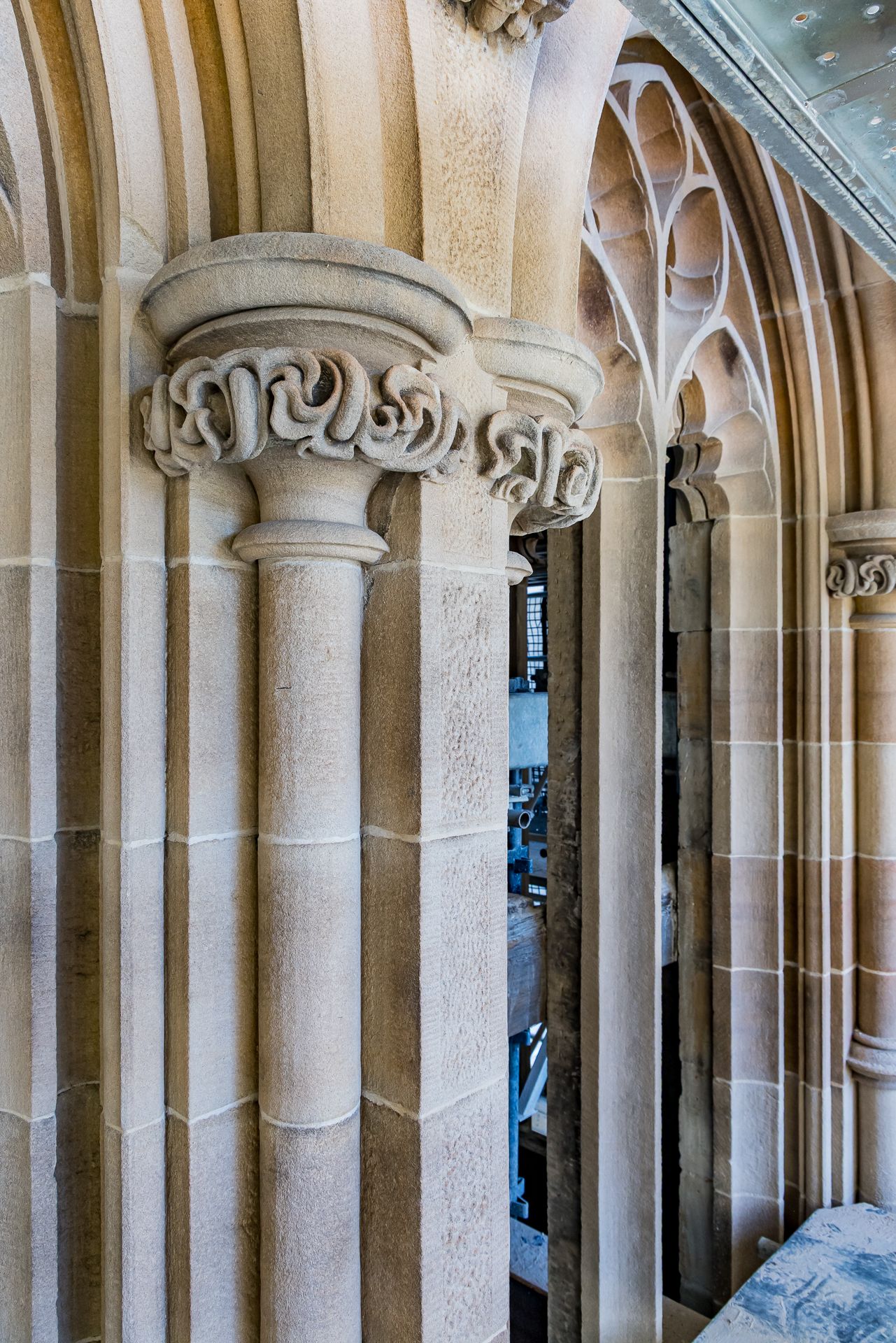 Gothic sandstone columns with carved scrolled capitals and tracery arches inside a historic stone tower.