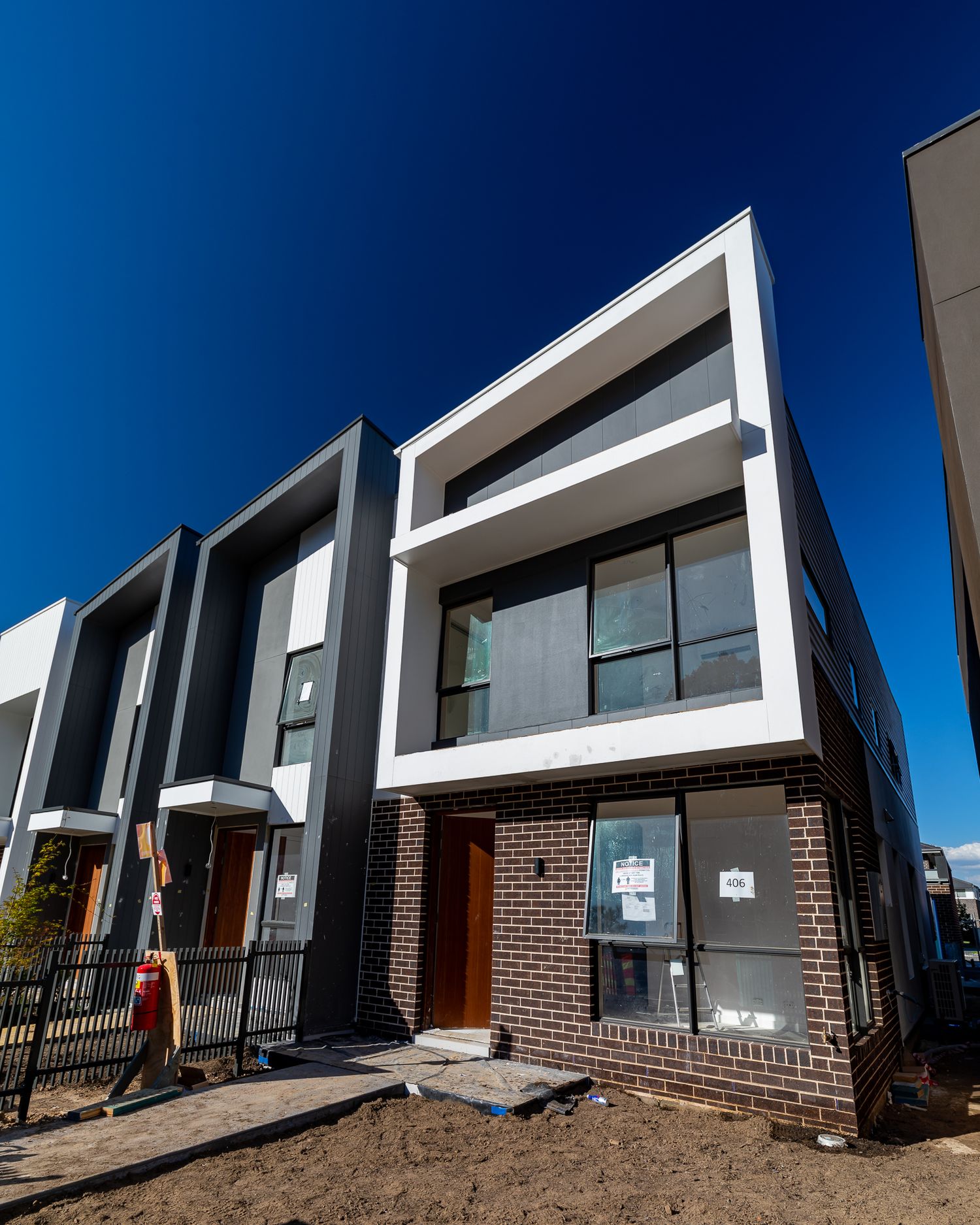 Modern two-storey townhouses with brick bases and contemporary white and grey facades under construction against a deep blue sky.