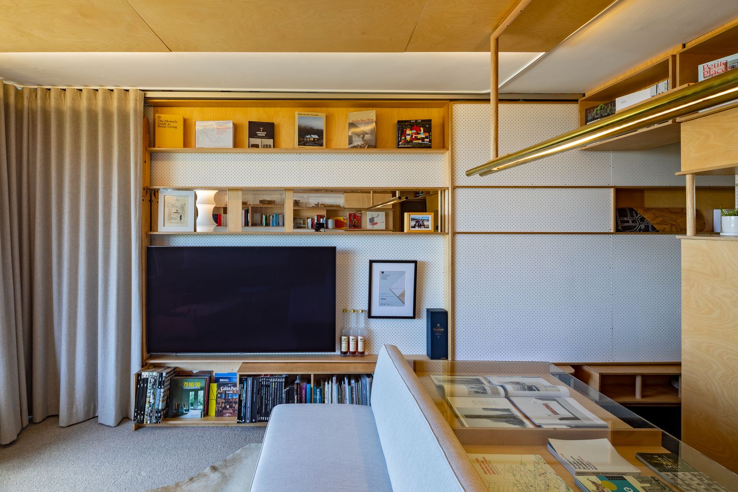 Contemporary living room with sliding white wall panels partly covering wooden shelves and a mounted television.