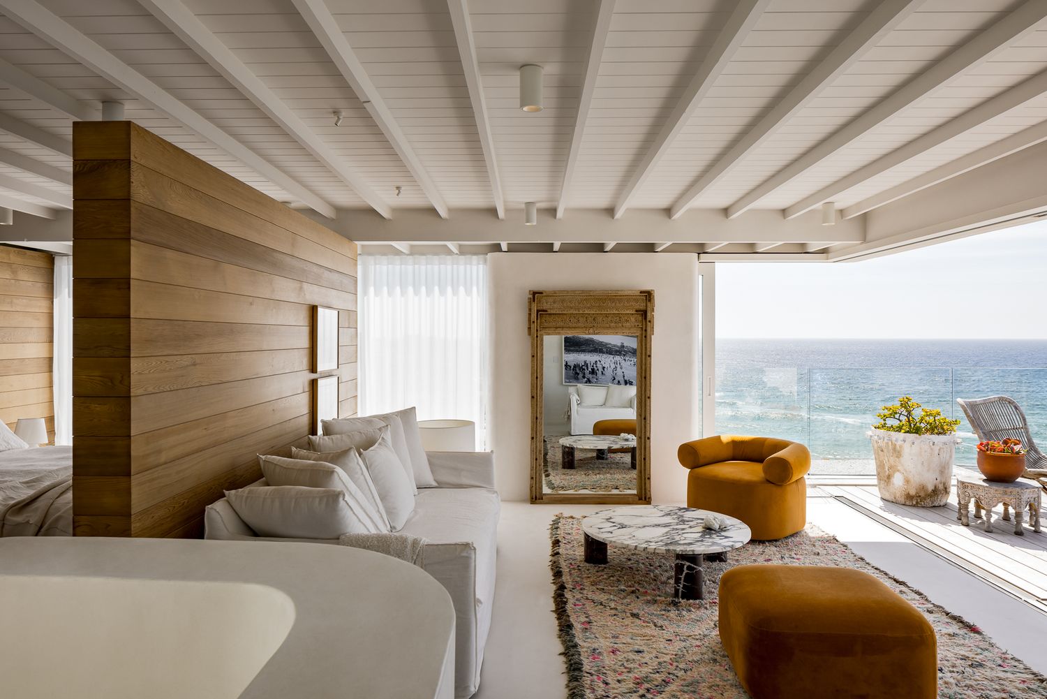 Coastal living room with white sofa, mustard armchair, timber feature wall and open sliding doors overlooking the ocean.