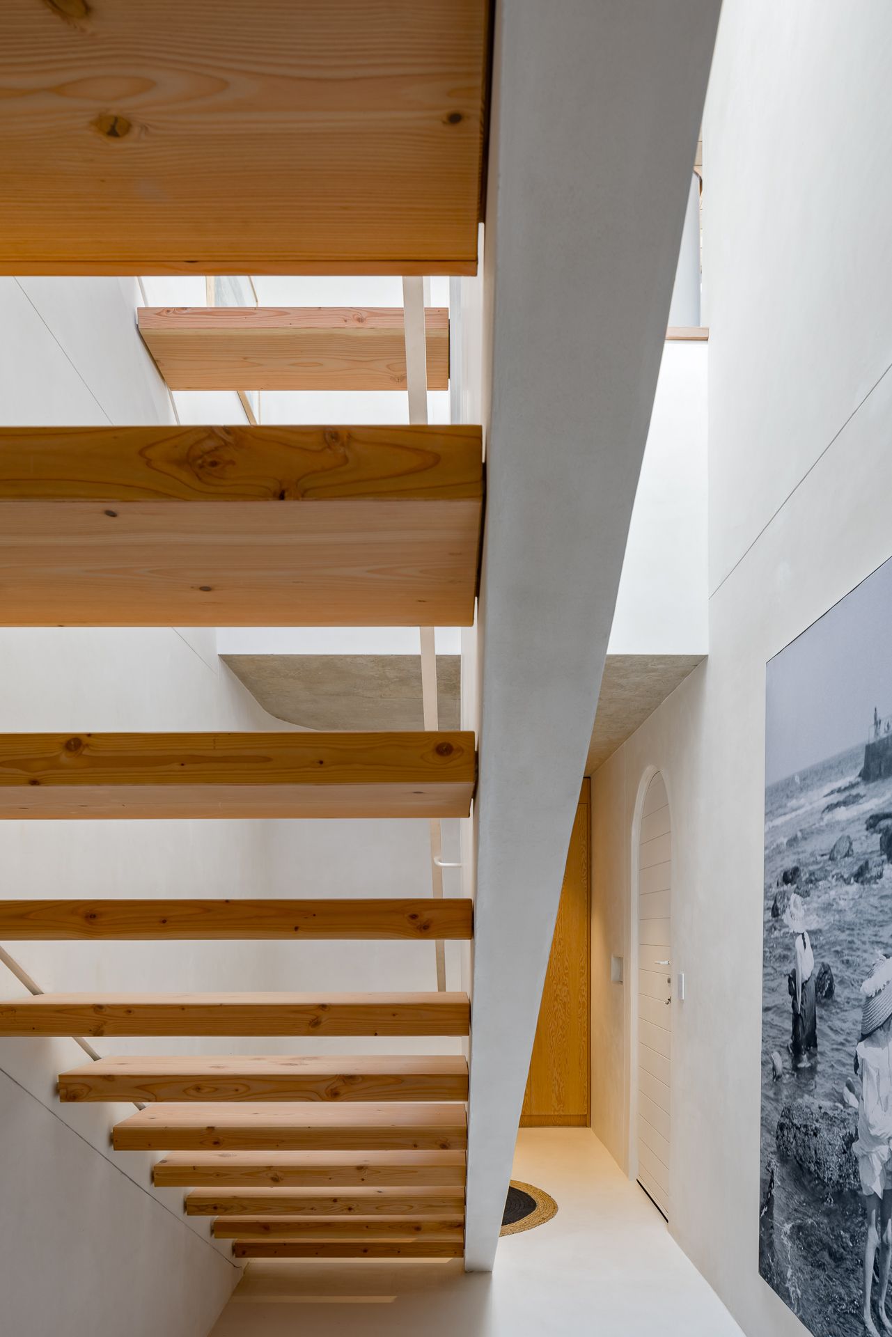 View up an open timber staircase with chunky wooden treads, white plaster walls and a large black-and-white photo mural.