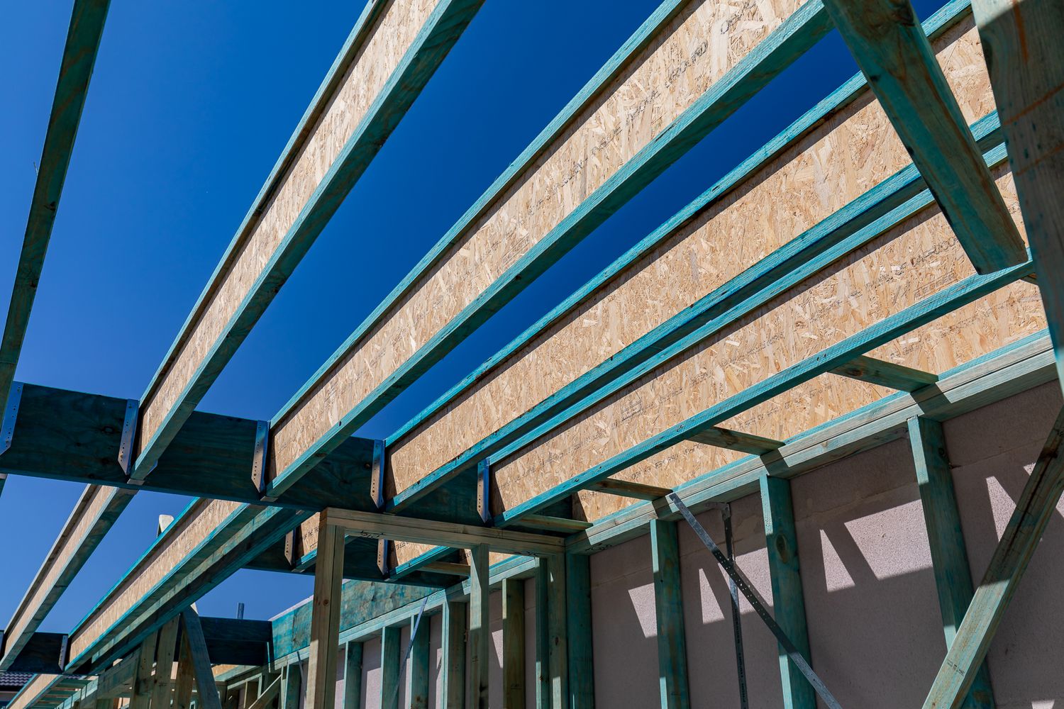 Close-up of timber roof trusses and steel framing against a bright blue sky on a residential building under construction.