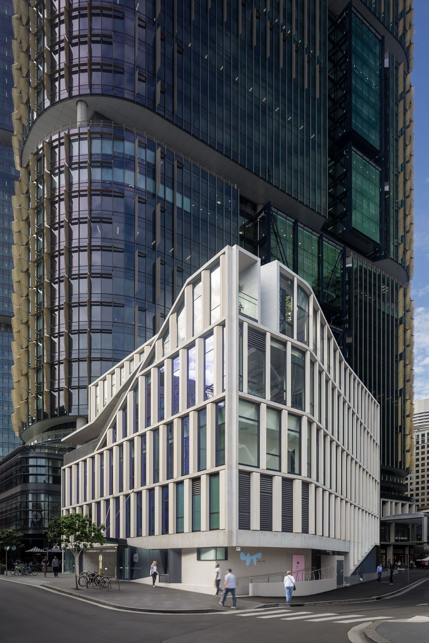 Modern white angular building with vertical windows standing at a street corner beside a curved glass skyscraper.