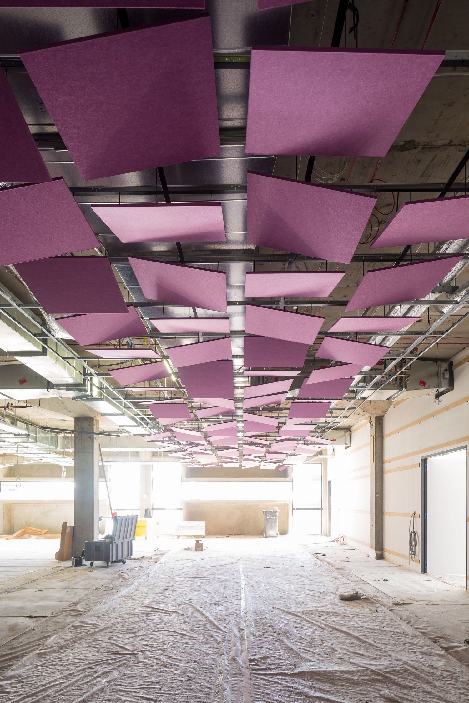Construction interior with suspended pink acoustic ceiling panels above a protected floor and exposed services.