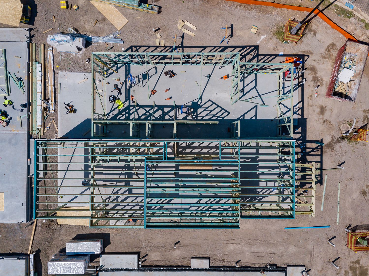 Aerial top-down view of a steel building frame under construction with beams, bracing, and workers on a cleared site.