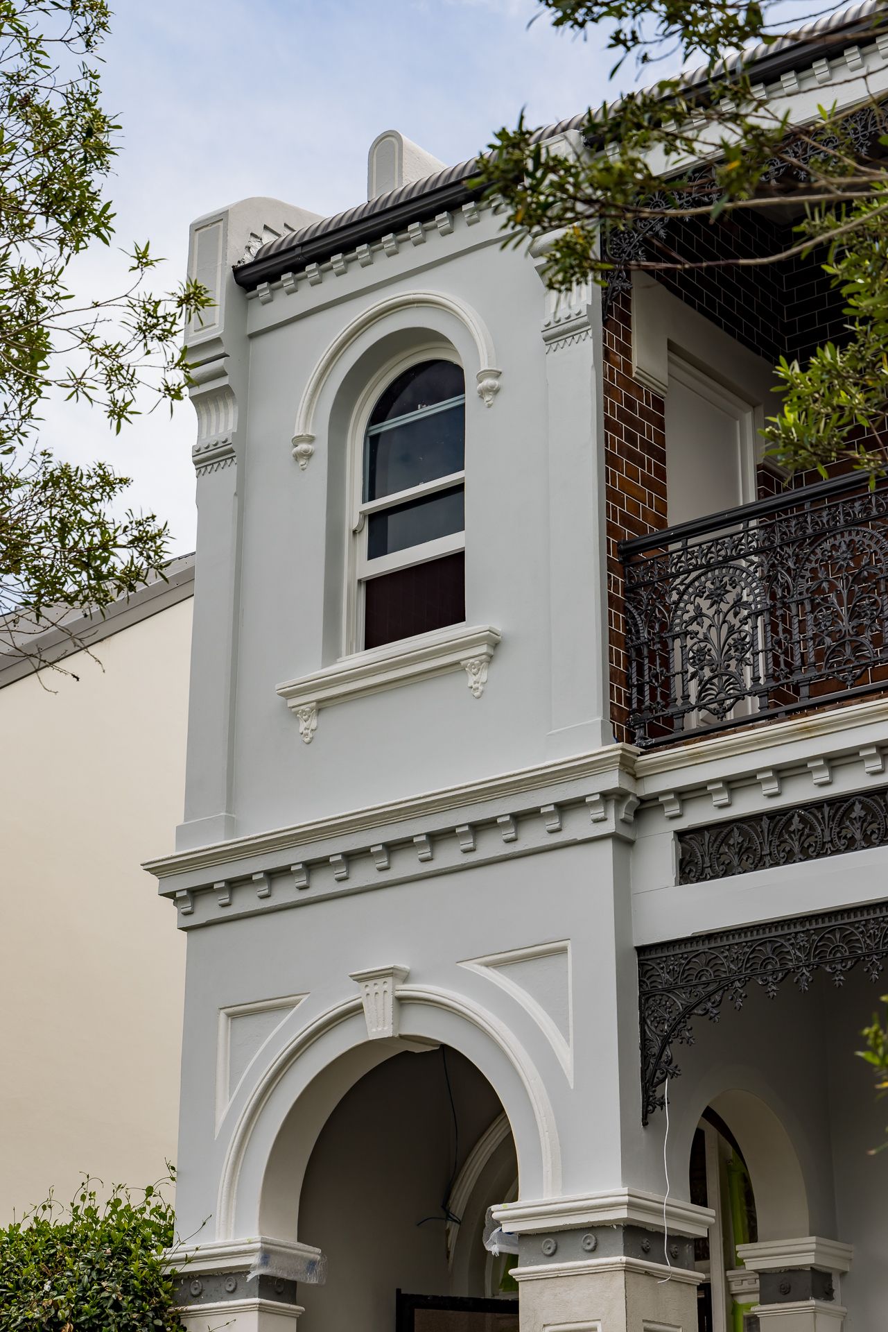Heritage terrace house with arched window, ornate cast iron lacework balcony, decorative cornices and a rounded entry archway.