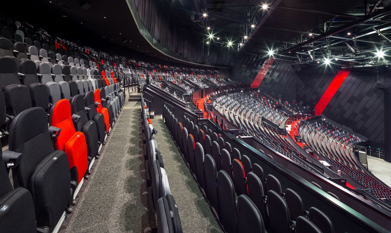 Rows of dark and red theatre seats rise in tiered levels inside a modern auditorium with accent lighting.