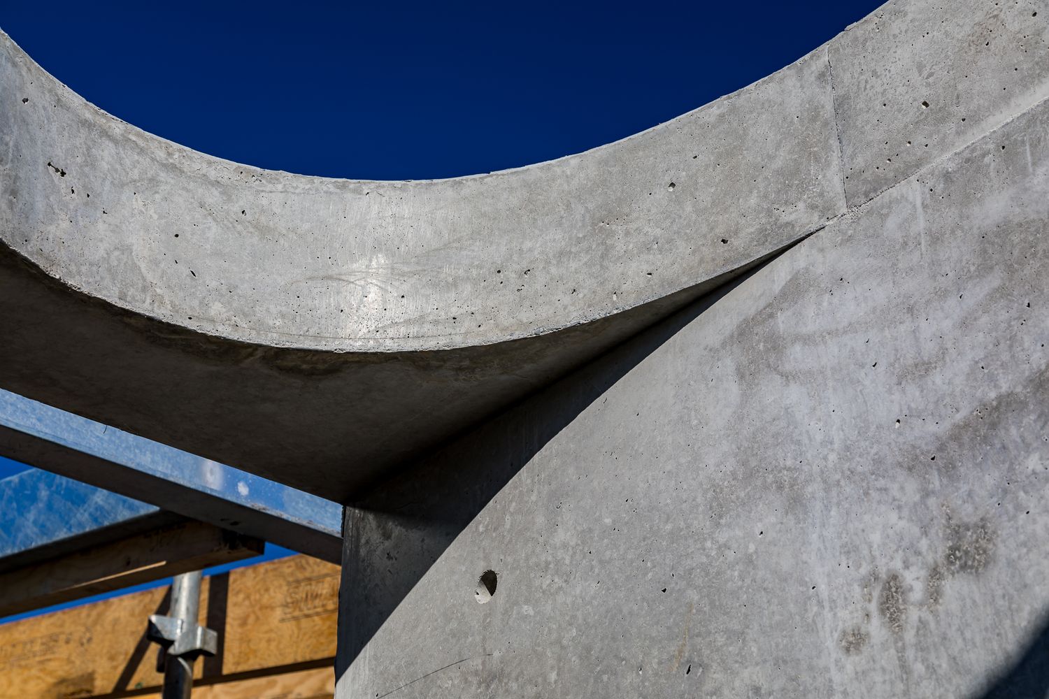 Curved raw concrete walls with a weathered texture and rounded edges set against a deep blue sky.