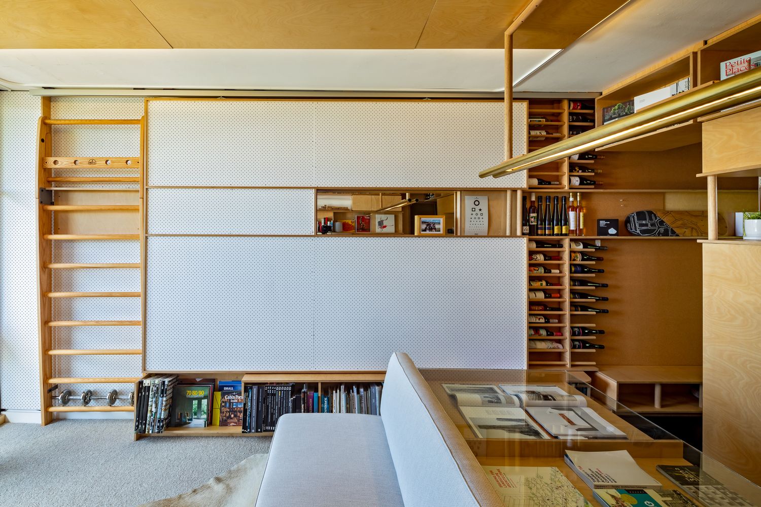 Modern home interior with wooden climbing wall bars, white acoustic panels and warm timber shelving units.
