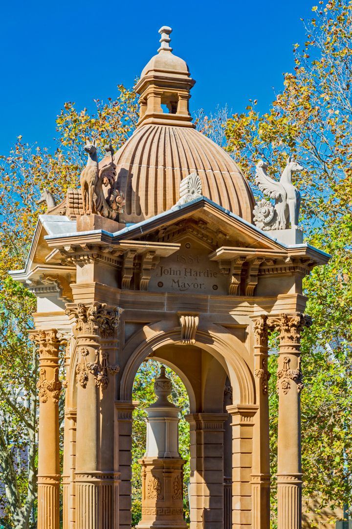 Ornate sandstone memorial fountain with a domed canopy, carved columns, winged sculptures and an inscription naming a mayor.