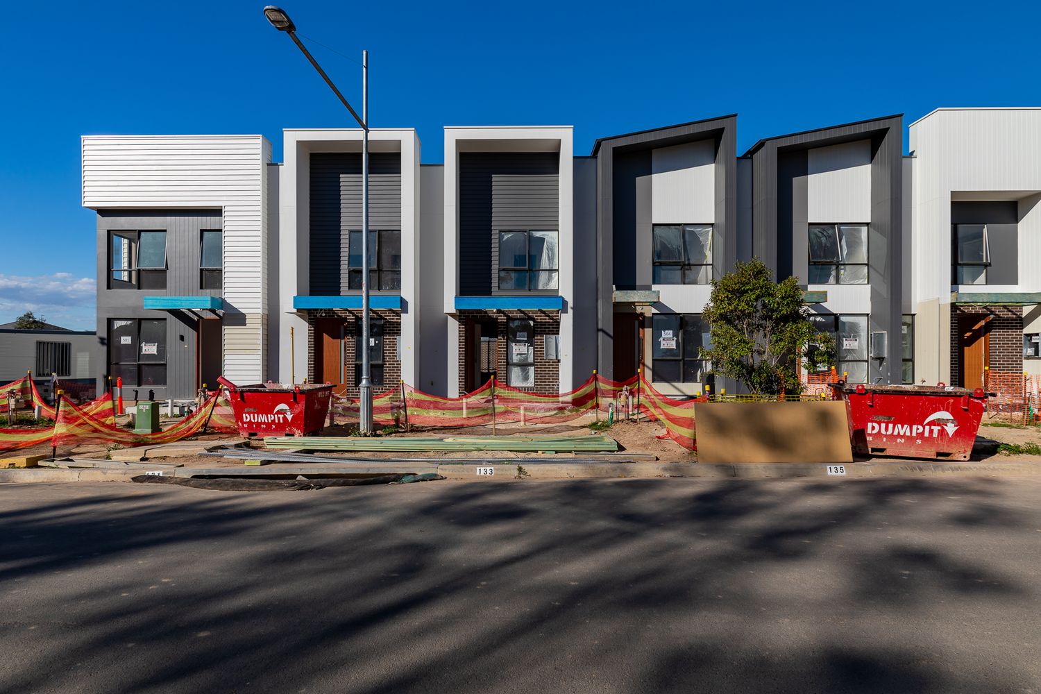 Row of modern townhouses with contemporary facades and orange safety fencing at a residential construction site on a sunny day.