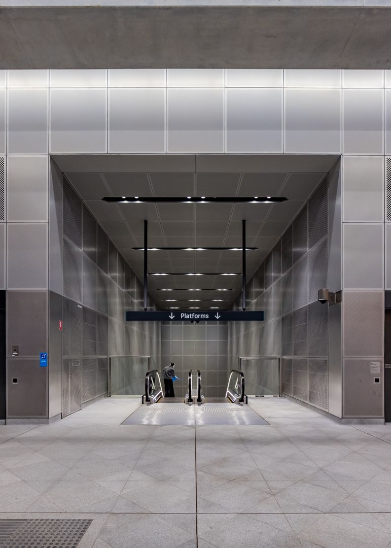 Sleek underground station entrance with metal paneled walls, escalators, and a Platforms sign above a polished stone floor.