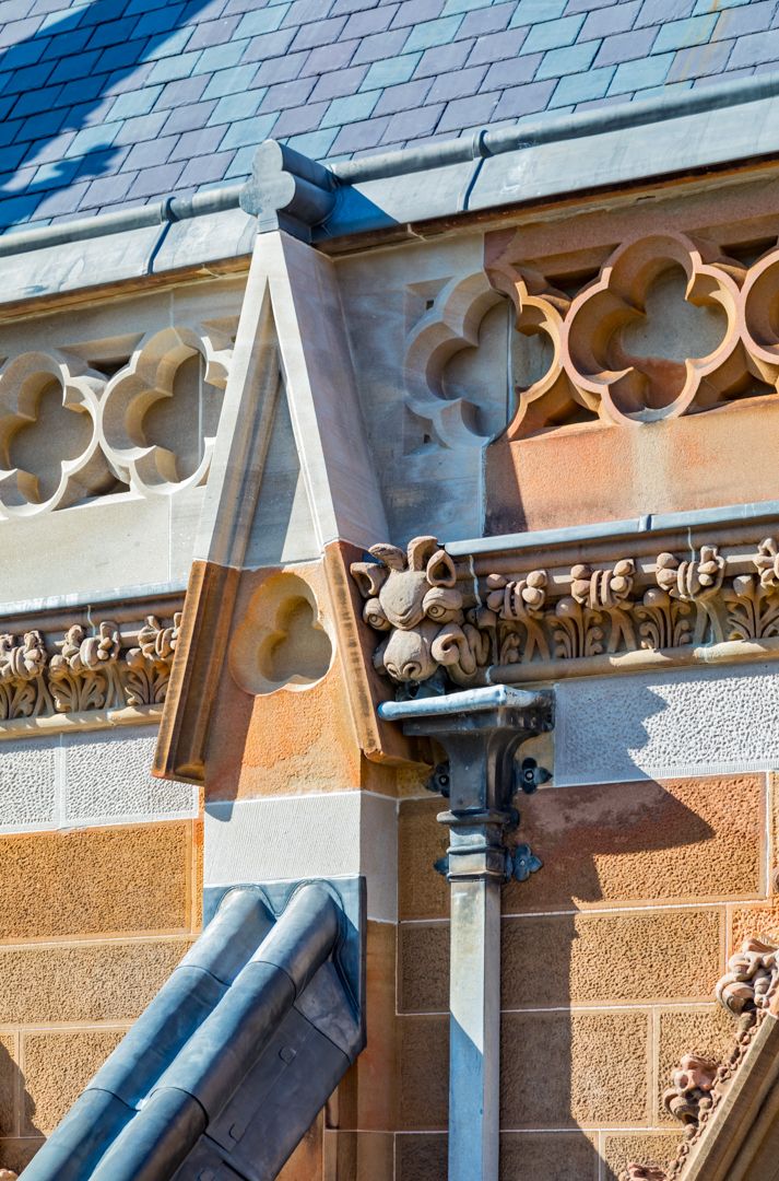 Close-up of ornate sandstone architectural details with carved Gothic stonework, decorative corbels and a slate roof edge.