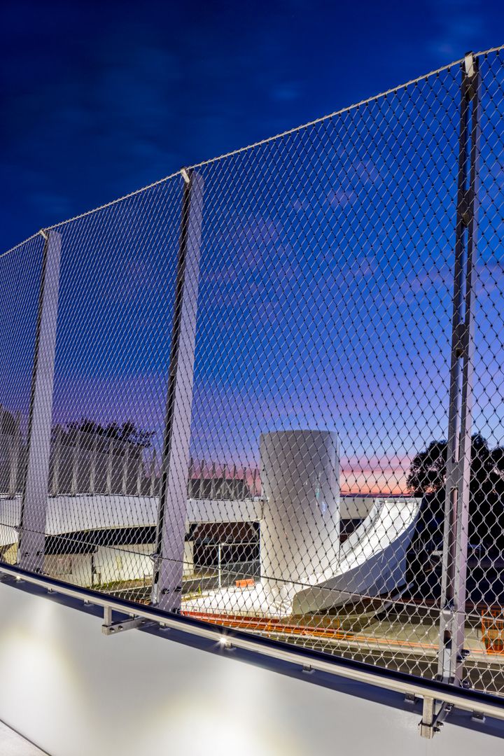 Steel mesh balustrade overlooks a white curved concrete structure and silhouetted trees against a vivid purple and blue twilight sky.