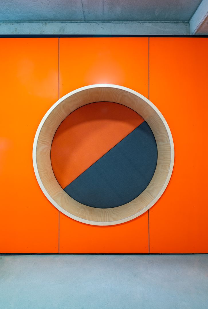 Bright orange wall panels with a circular wooden-framed porthole featuring a diagonal orange and gray split design.