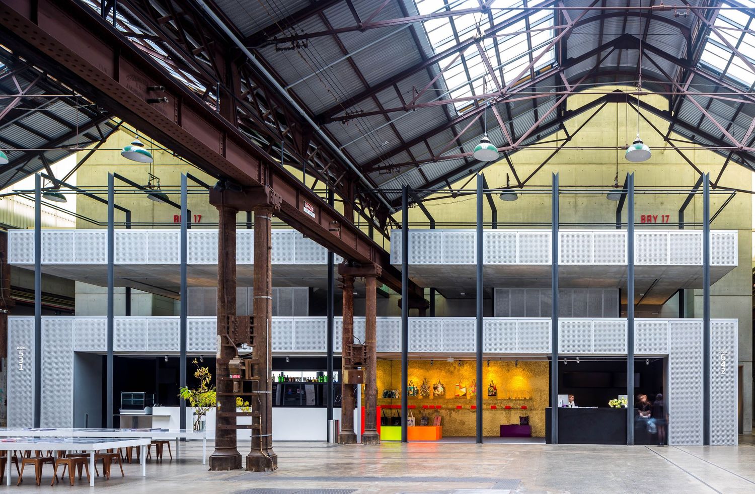 Renovated industrial hall with exposed steel beams, a glass skylight roof and a modern multi-level office structure inside.