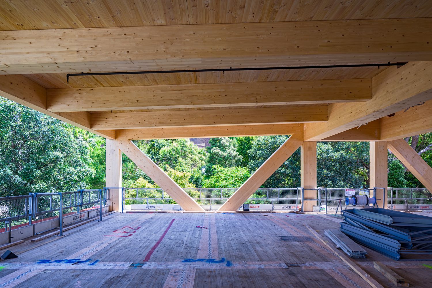 Timber-framed building structure with diagonal wooden supports and exposed beams, overlooking lush green trees.