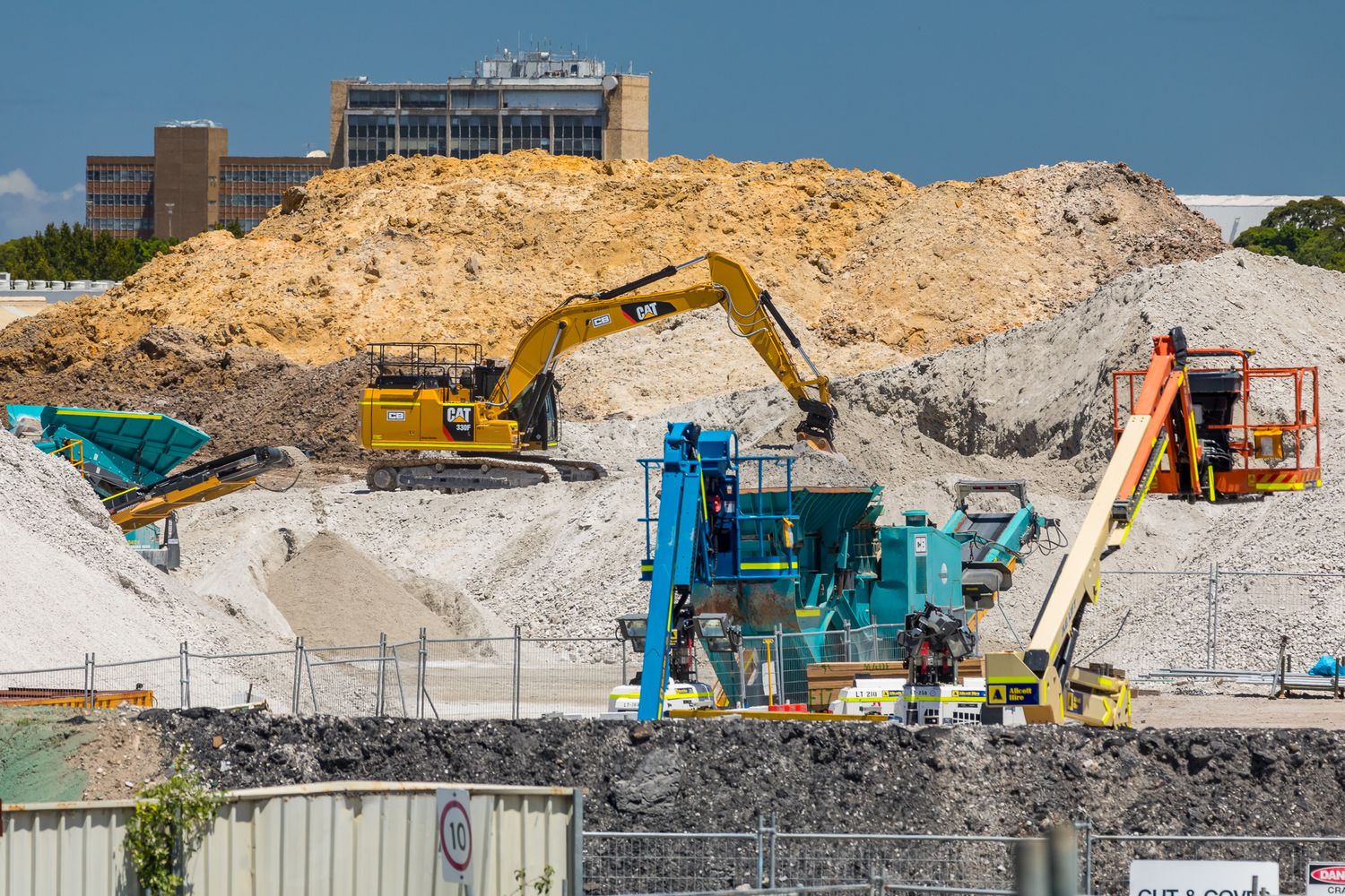 Yellow excavator and heavy machinery working on large mounds of sand and rubble at an earthmoving construction site.