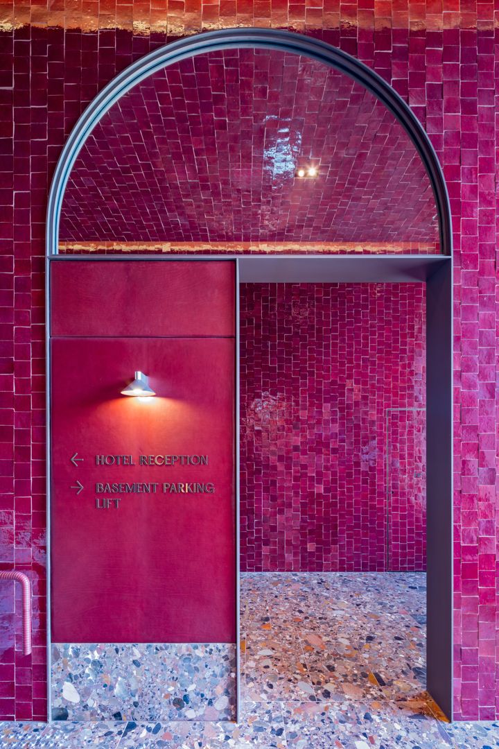 Arched doorway clad in glossy magenta tiles with a wall sign pointing to hotel reception, basement parking and lift above terrazzo flooring.