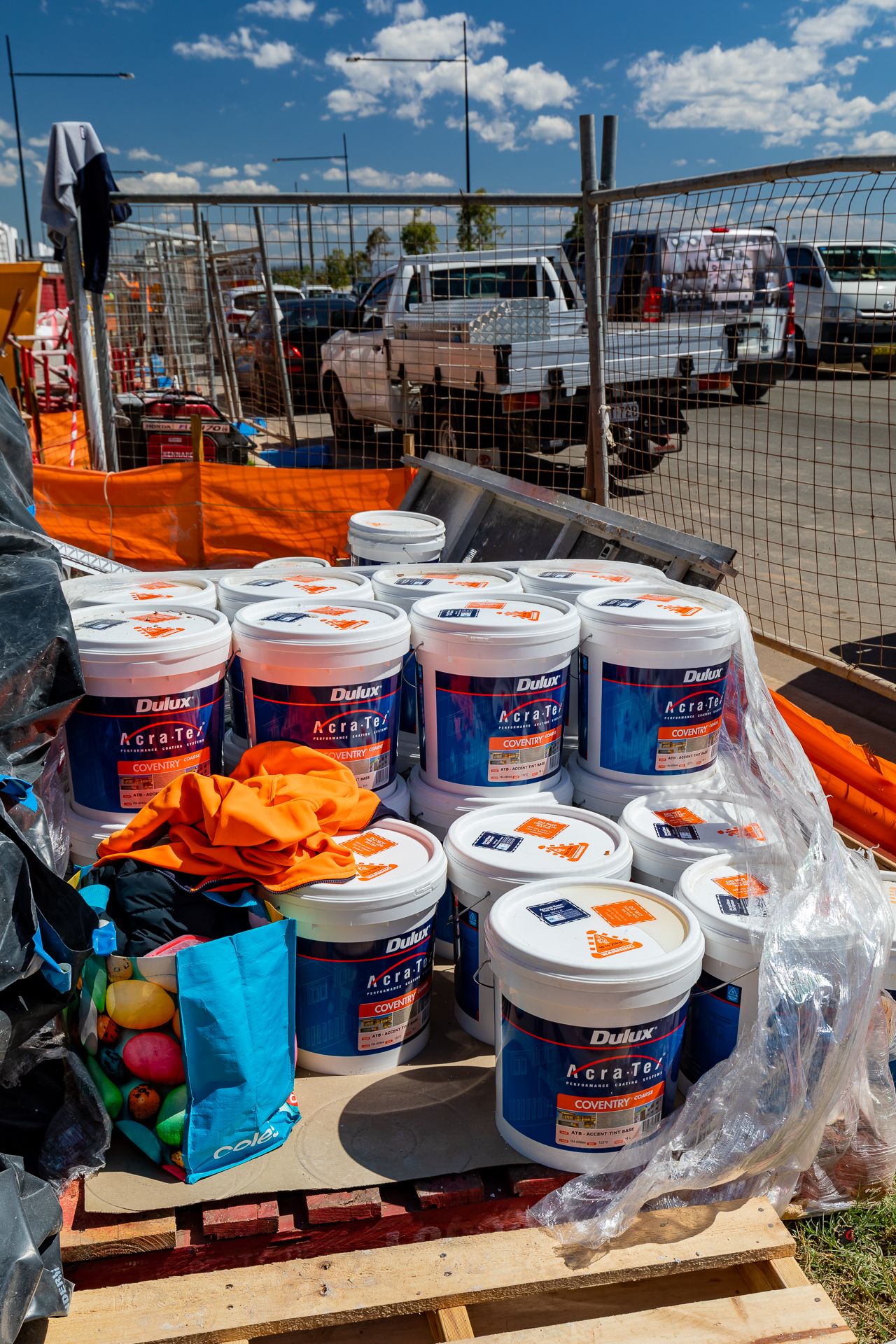 Pallet of Dulux AcraTex paint buckets on a construction site, with a utility vehicle and mesh fencing in the background.