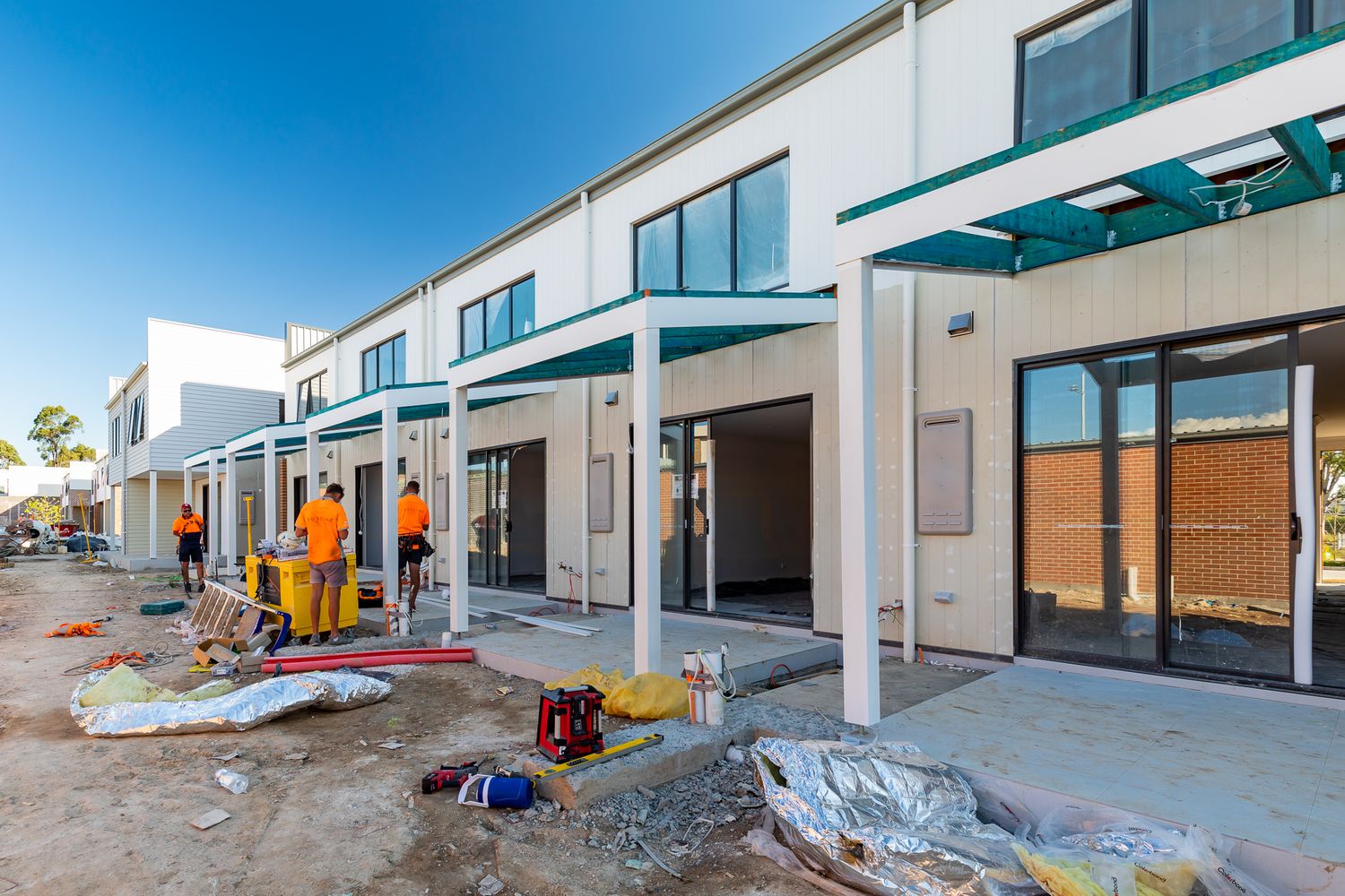 Construction workers in orange hi-vis clothing building covered entry porches on a new row of modern townhouses.