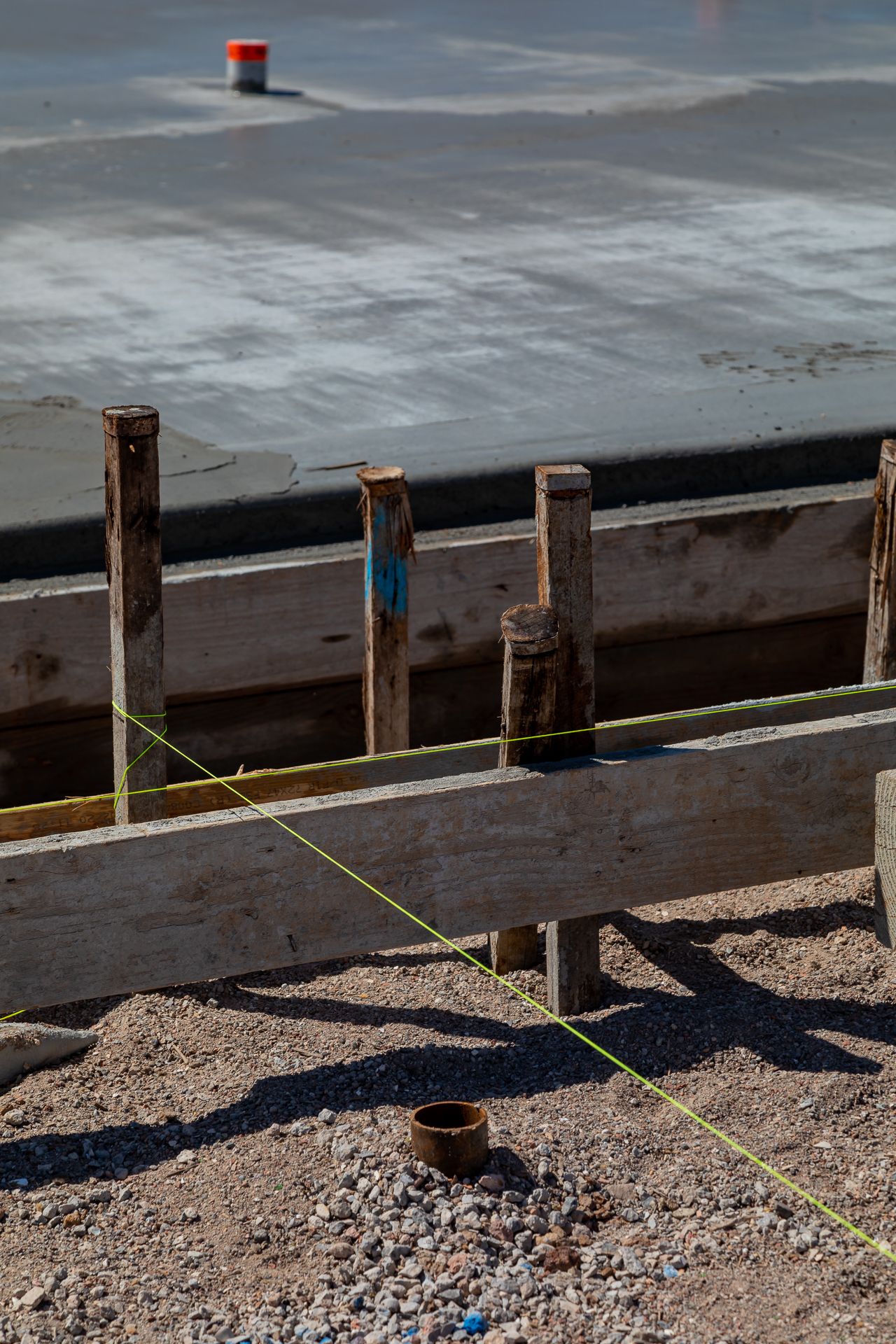 A wet concrete slab edged by timber formwork and stakes, with a string line marking the boundary on a building site.