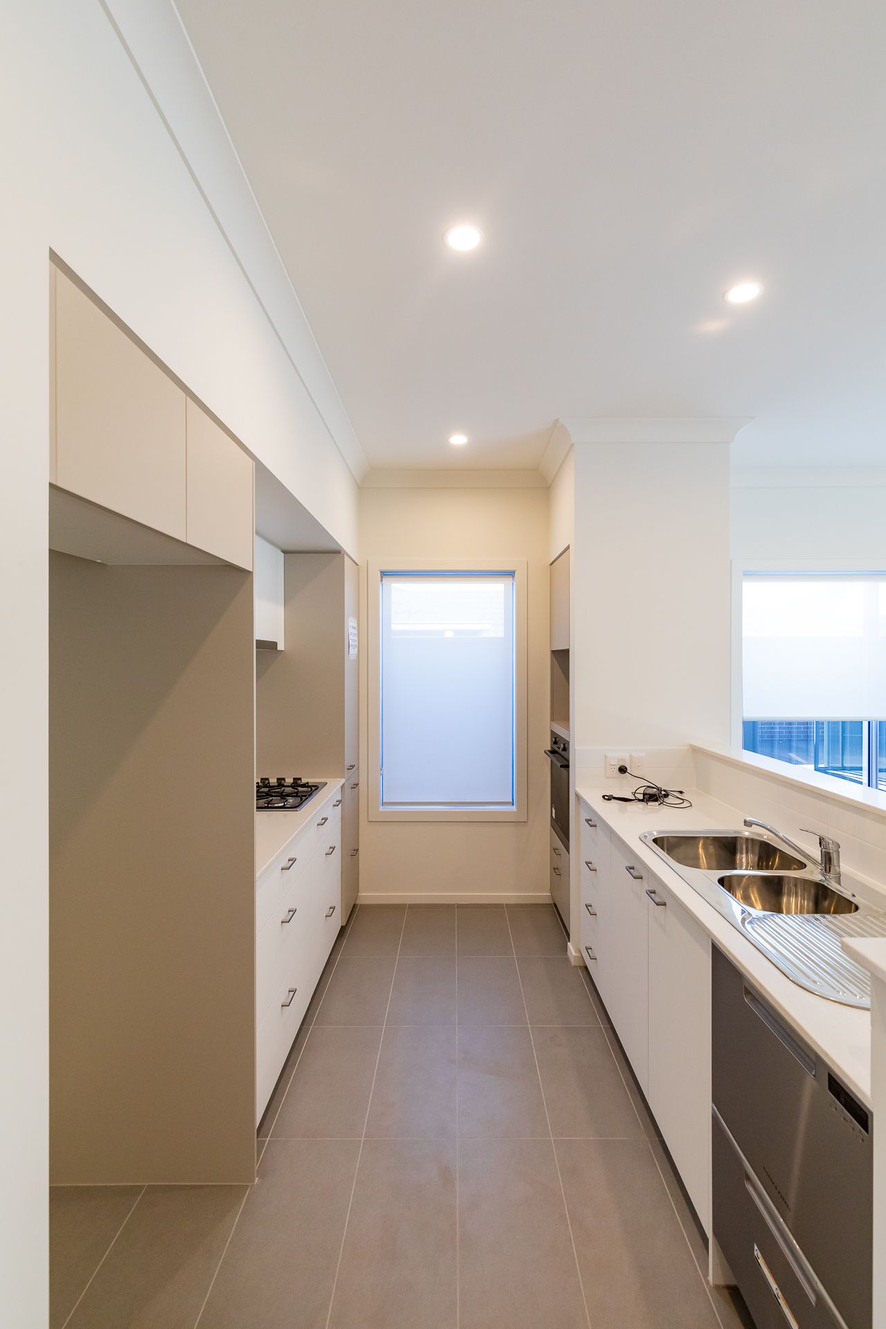 Bright galley kitchen in a new home with white cabinetry, stainless steel sink, gas cooktop, tiled floor and recessed lighting.