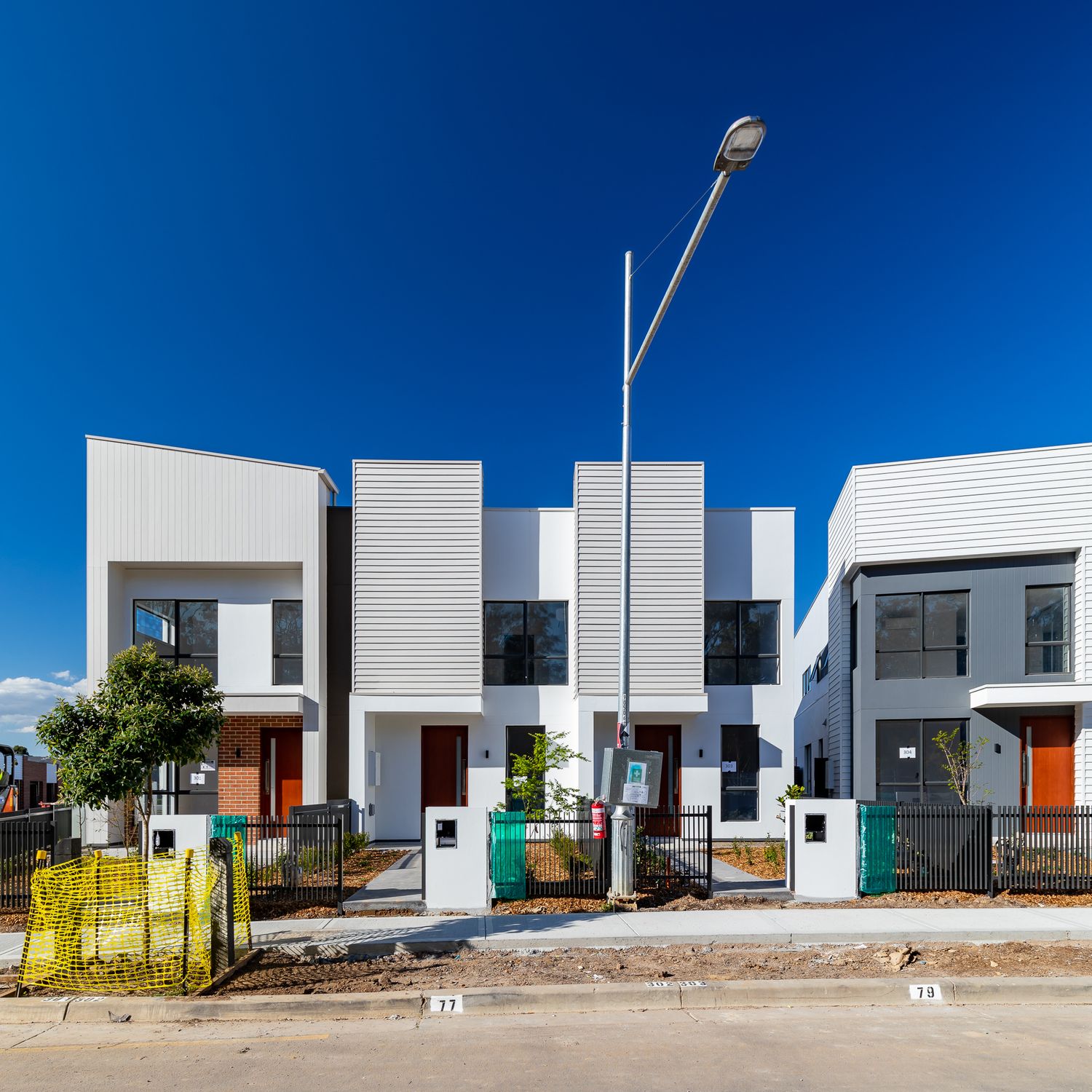 Row of newly built modern white and grey townhouses with orange front doors and a street lamp under a deep blue sky.