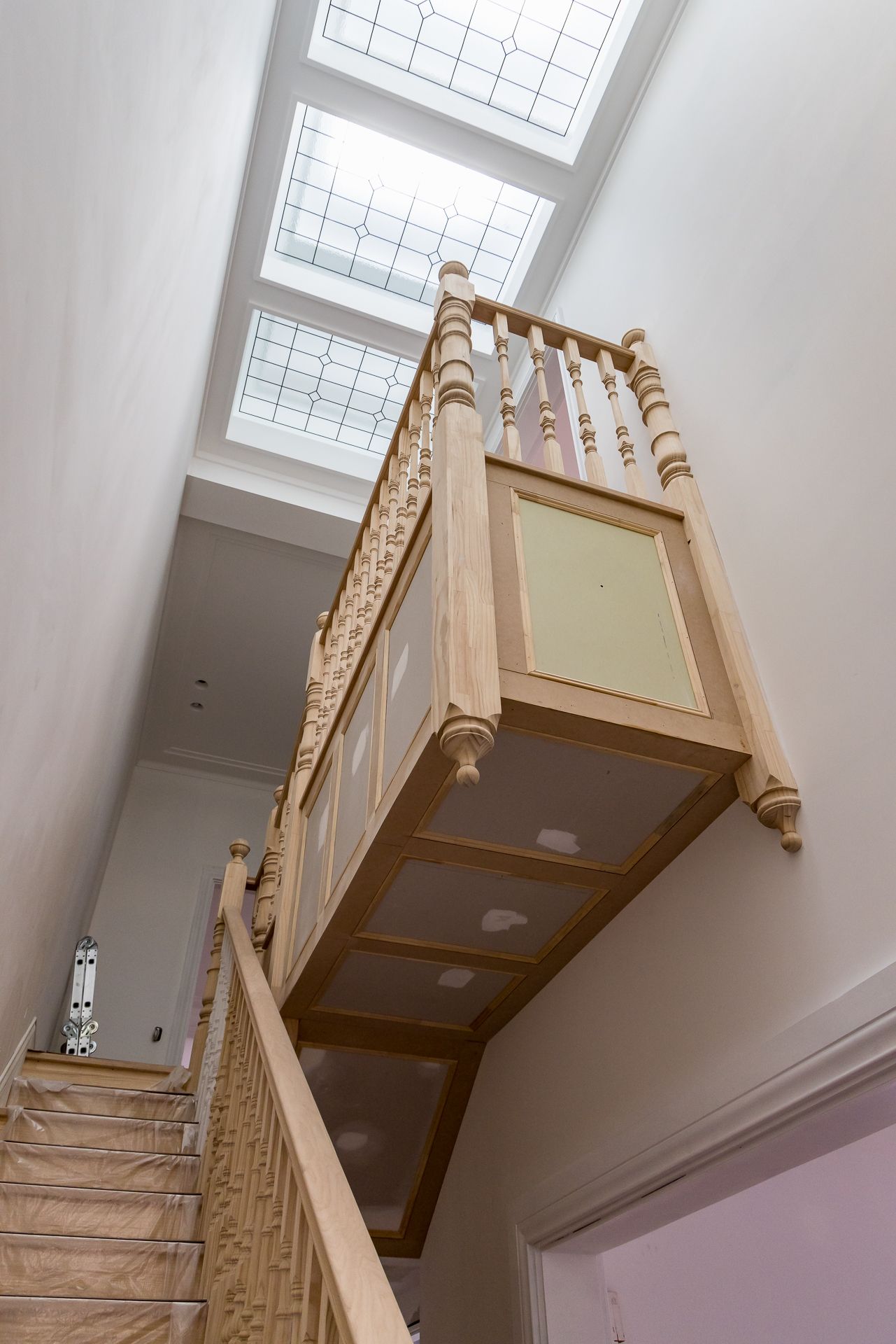 Looking up a timber staircase with turned balusters and a suspended landing beneath a leadlight skylight.