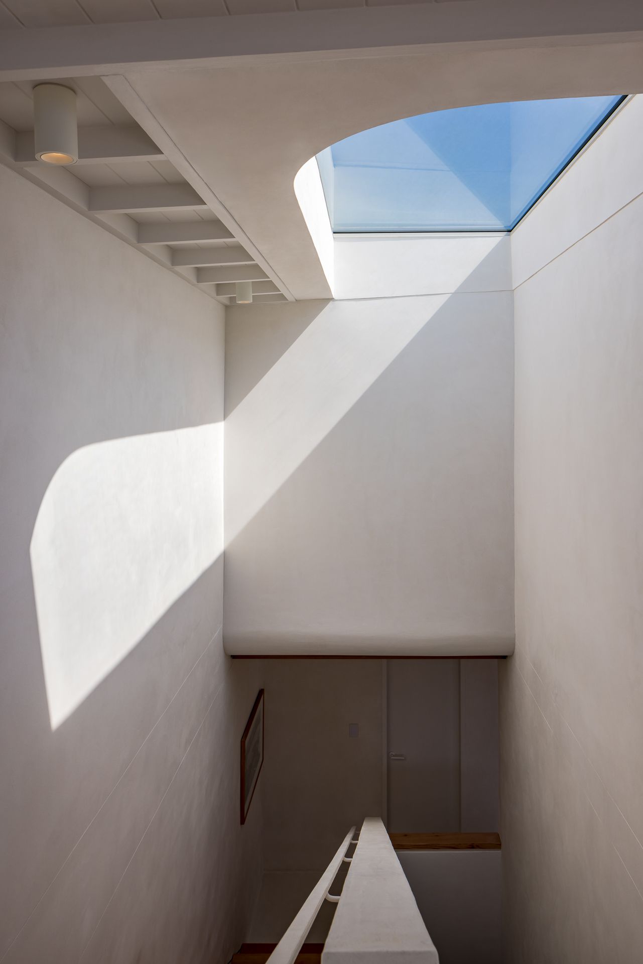 Minimalist white stairwell with a skylight casting soft geometric sunlight and shadows on the walls.