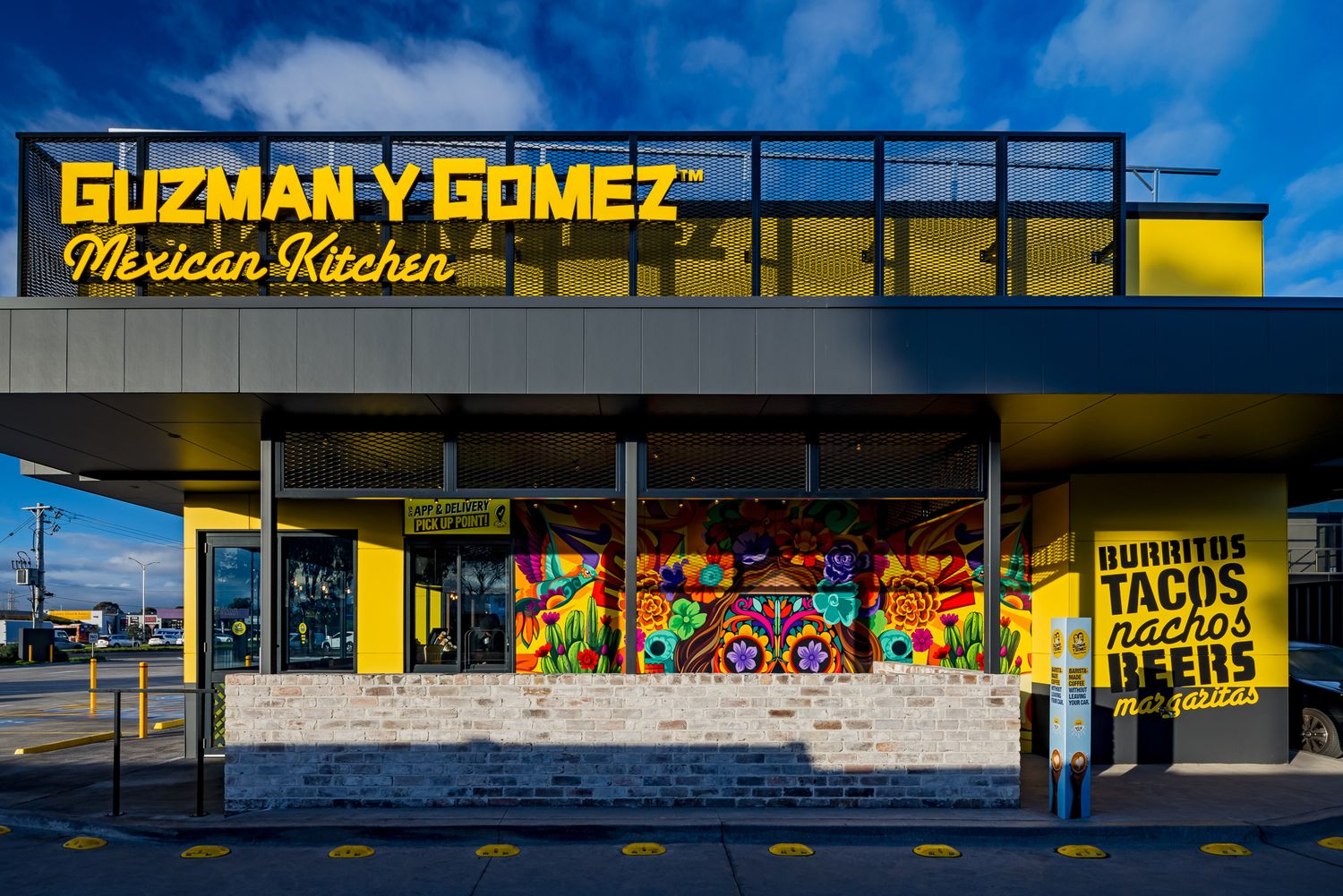 Guzman y Gomez Mexican Kitchen restaurant exterior at dusk with yellow signage and a menu of burritos, tacos, nachos and beers.