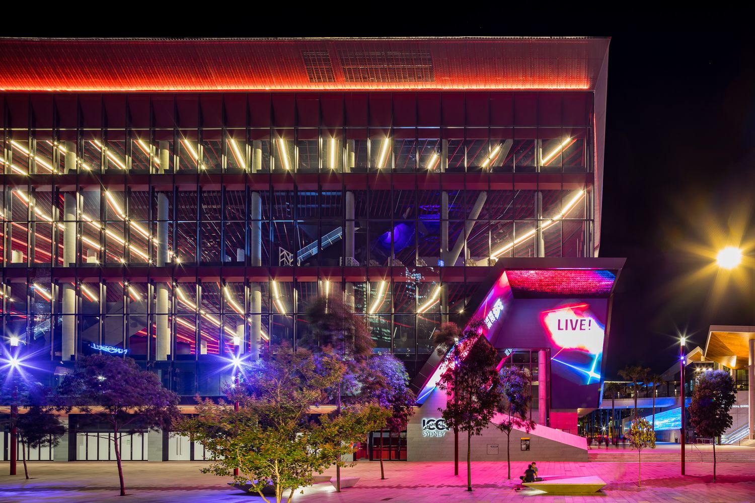 Illuminated modern convention centre with glowing orange light strips and a neon LIVE sign at night.