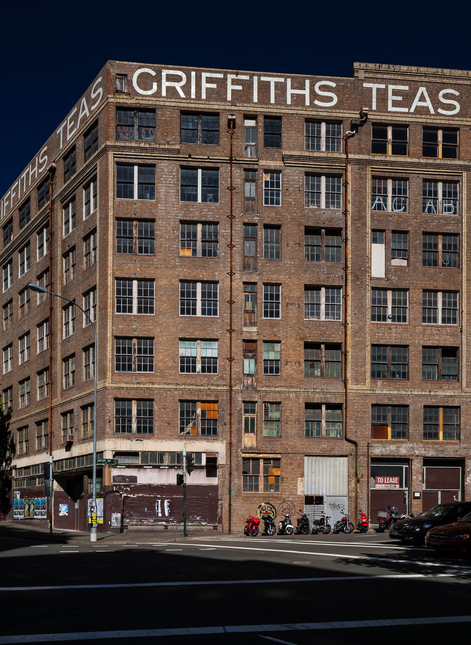 Historic multi-story brick Griffiths Teas warehouse building with large rooftop signage, many windows, and parked scooters on the street.