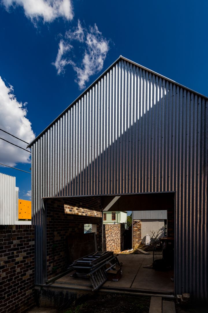 Corrugated metal clad building under construction with an open brick-lined entry, rubble and materials beneath a deep blue sky.