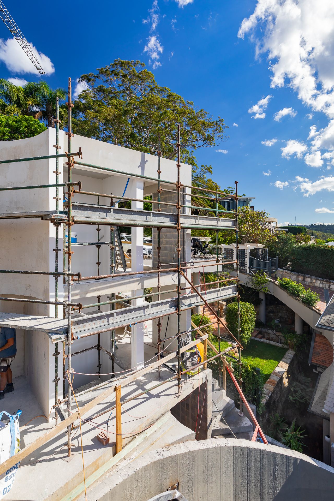 Multi-level residential building under construction with scaffolding, concrete walls and green gardens under a blue sky.